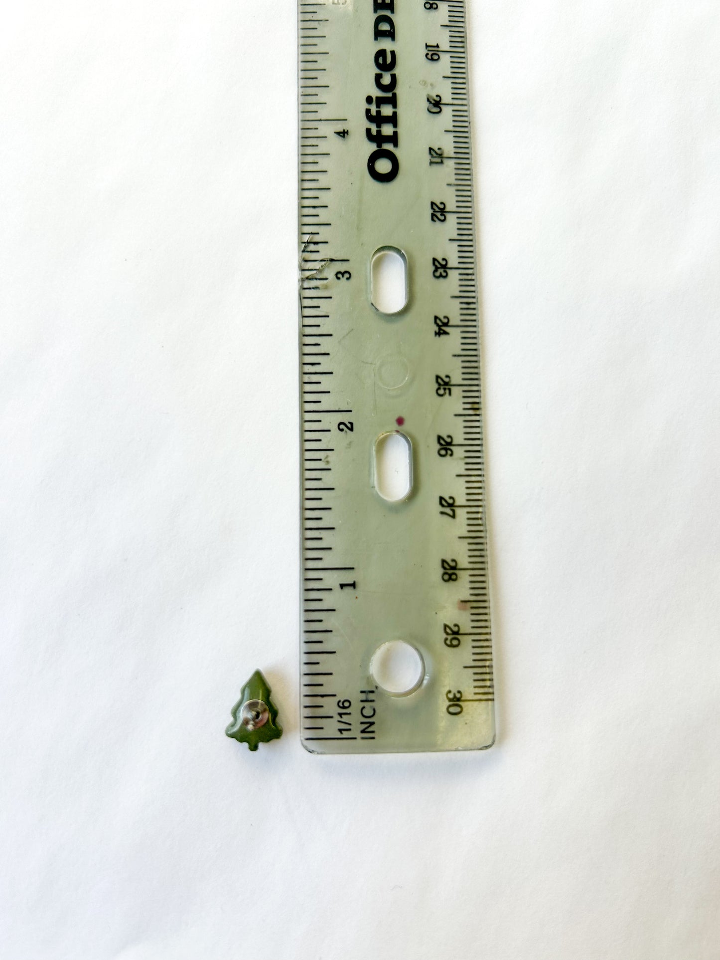 Small green tree stud next to a ruler on a white background