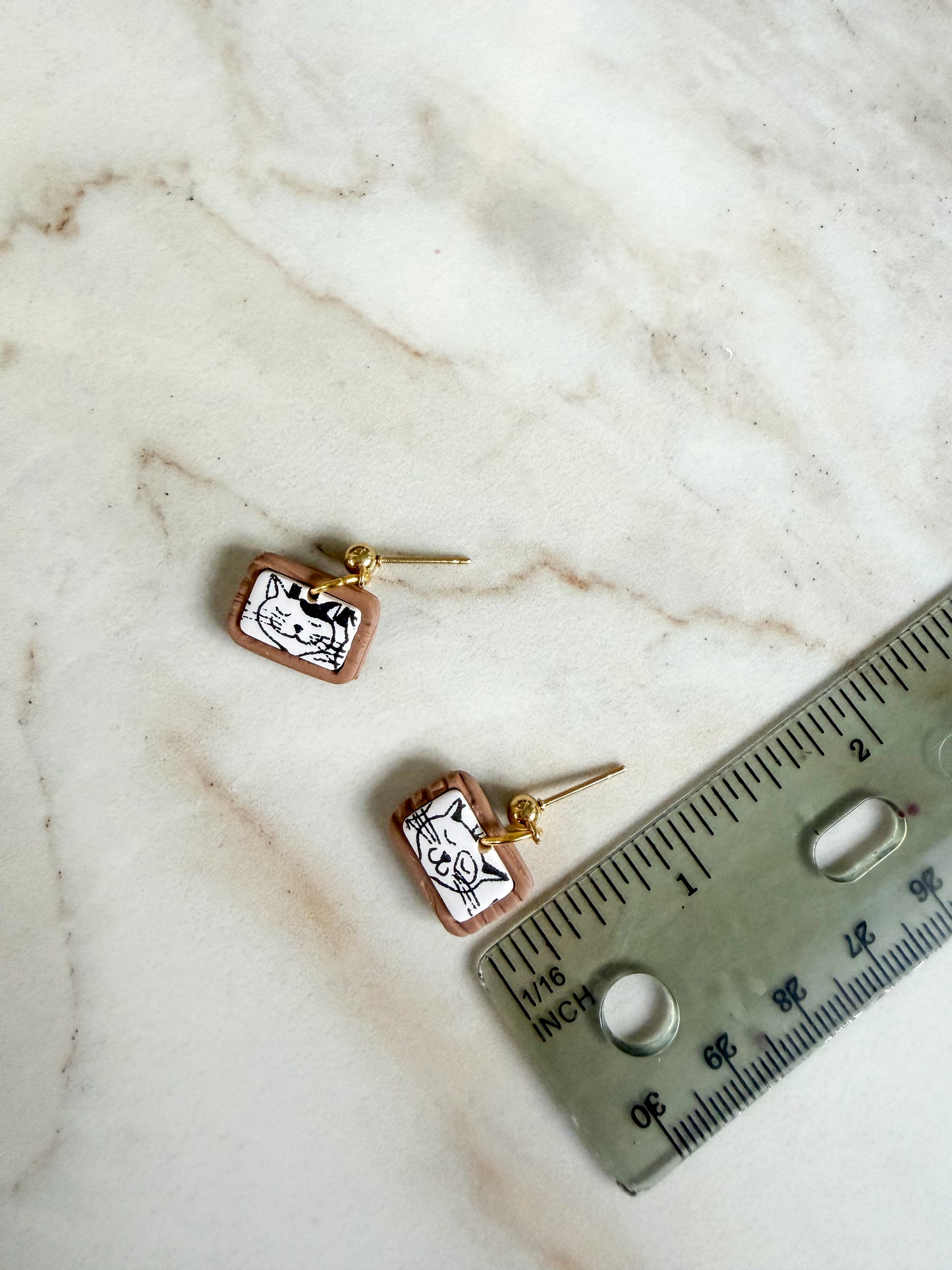 Pair of small gold earrings on a marble surface with a ruler for scale. 1/2 inch long