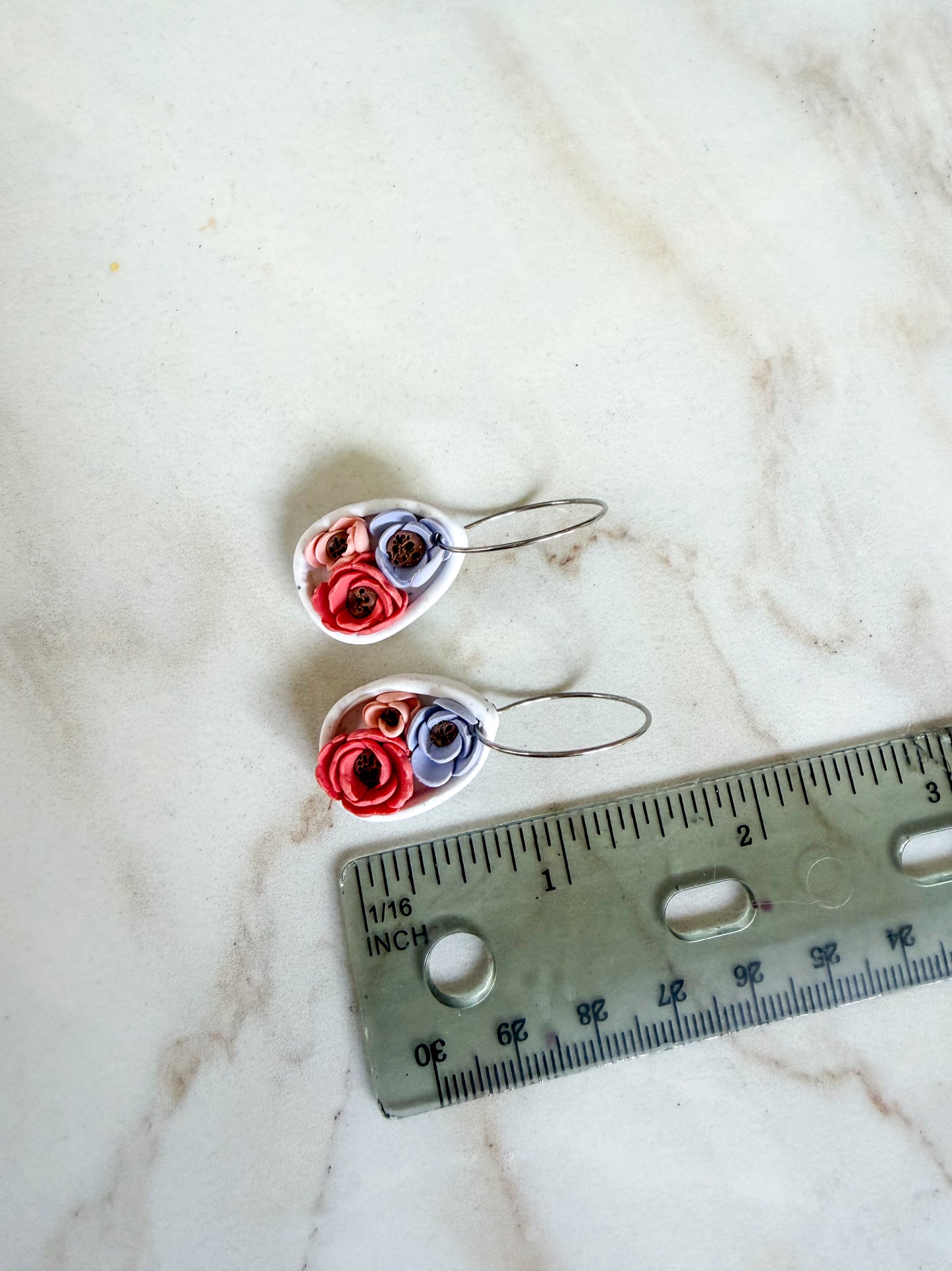 Heart-shaped earrings with floral designs on a marble surface with a ruler for scale. About 1.5 inches long