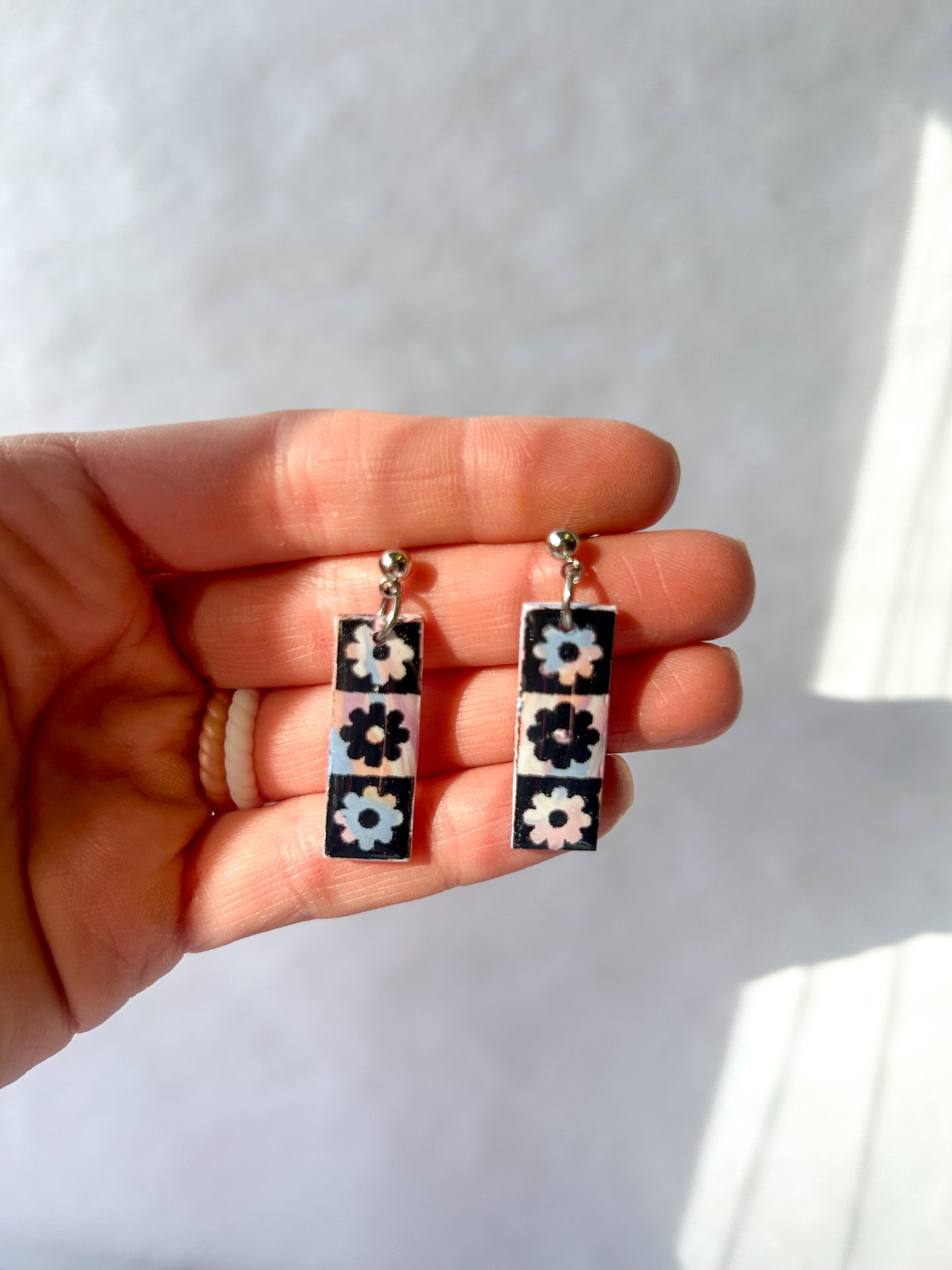 Hand holding two floral patterned earrings against a white background
