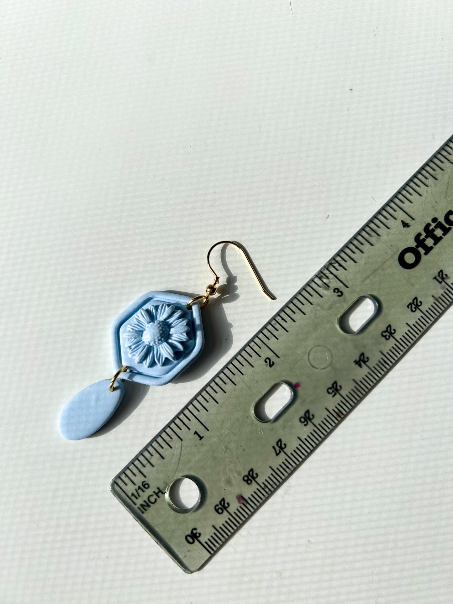Blue monochromatic hexagon shaped earrings with a daisy in the center. Next to a ruler for scale- about 2.5 inches in length
