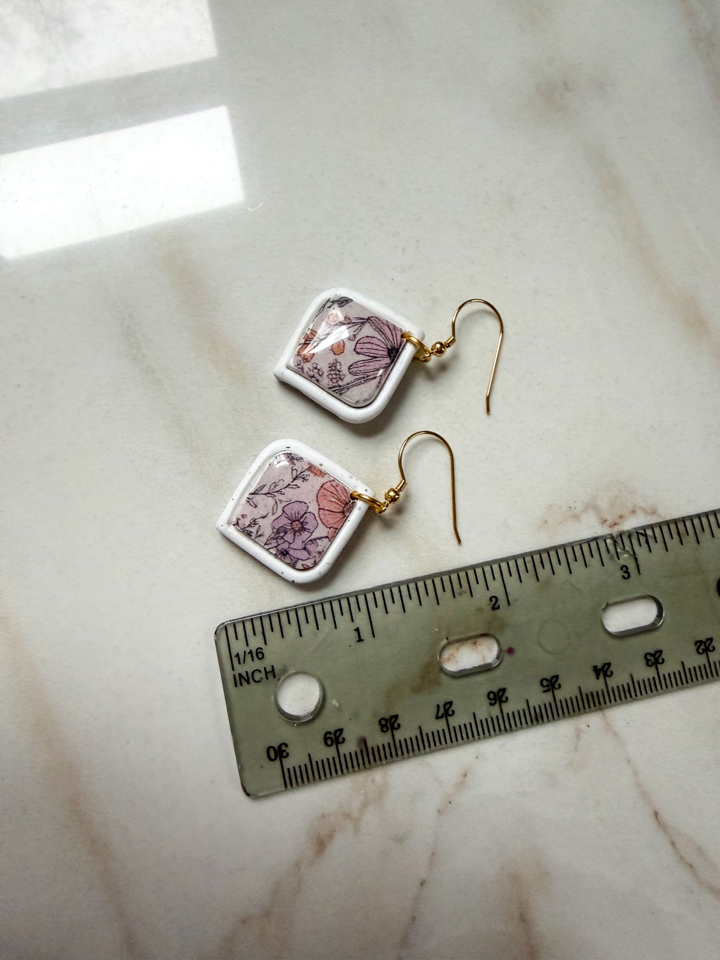 Pair of floral earrings on a marble surface with a ruler for scale. A little under 2 inches in length.