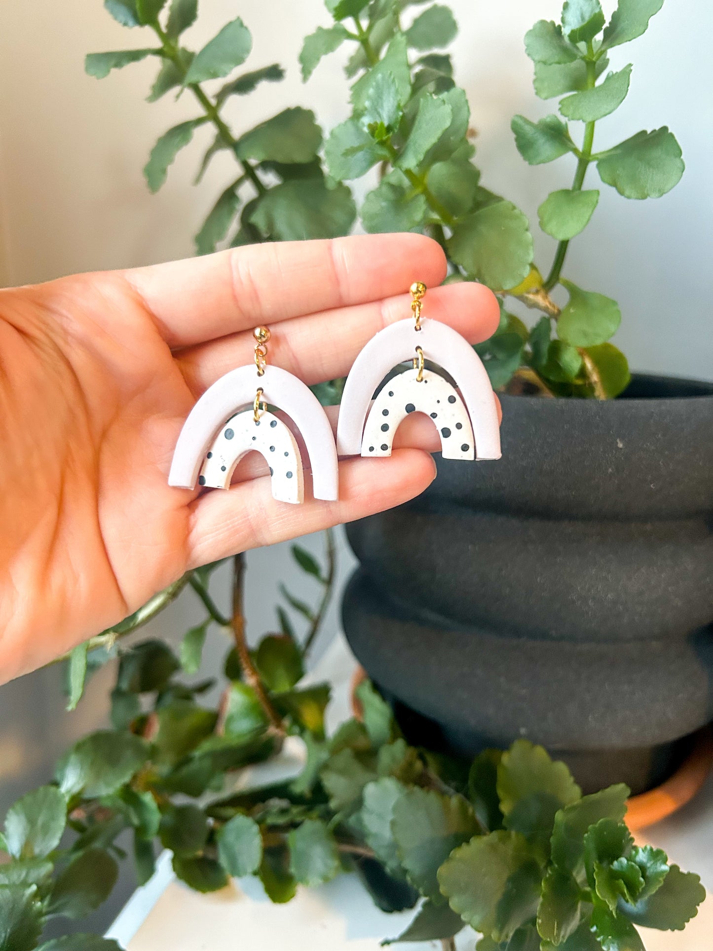 Double rainbow shaped dangles. The tops are light purple and the bottoms are polkadot. Held in a hand.