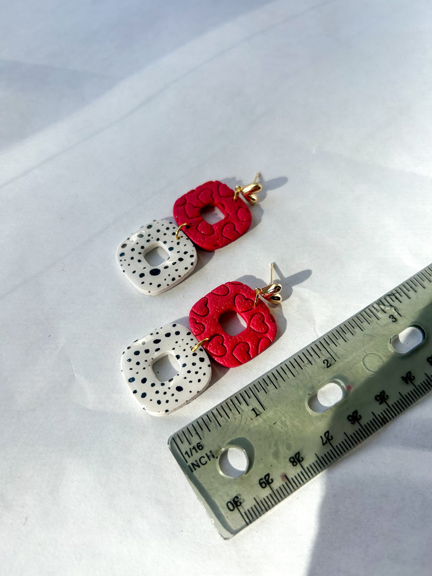 Pair of earrings with red floral designs and white textured circles, next to a ruler for scale on a white background. 2 inches in length.