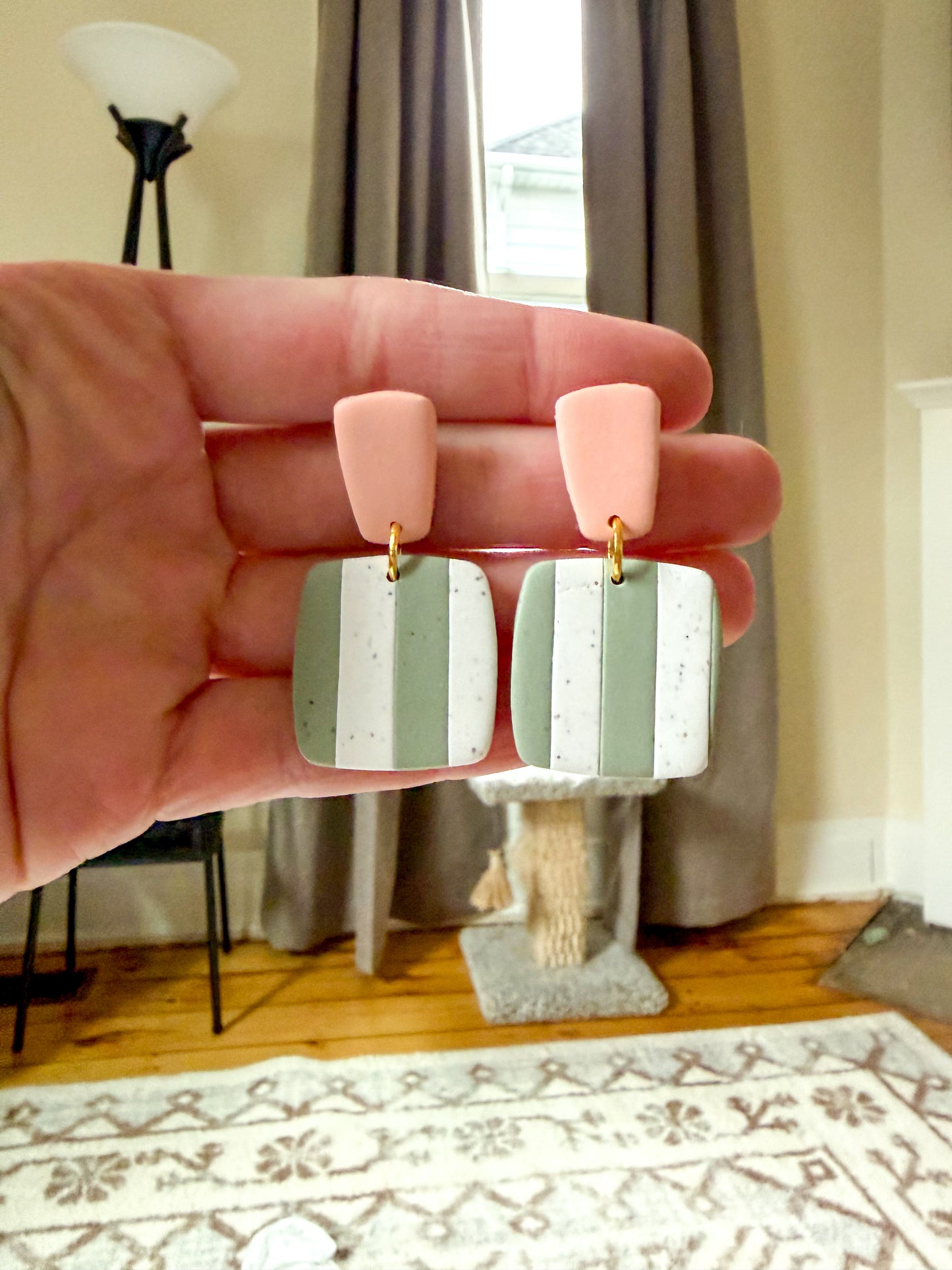 Hand holding a pair of earrings with pink tops and striped green and white bottoms.