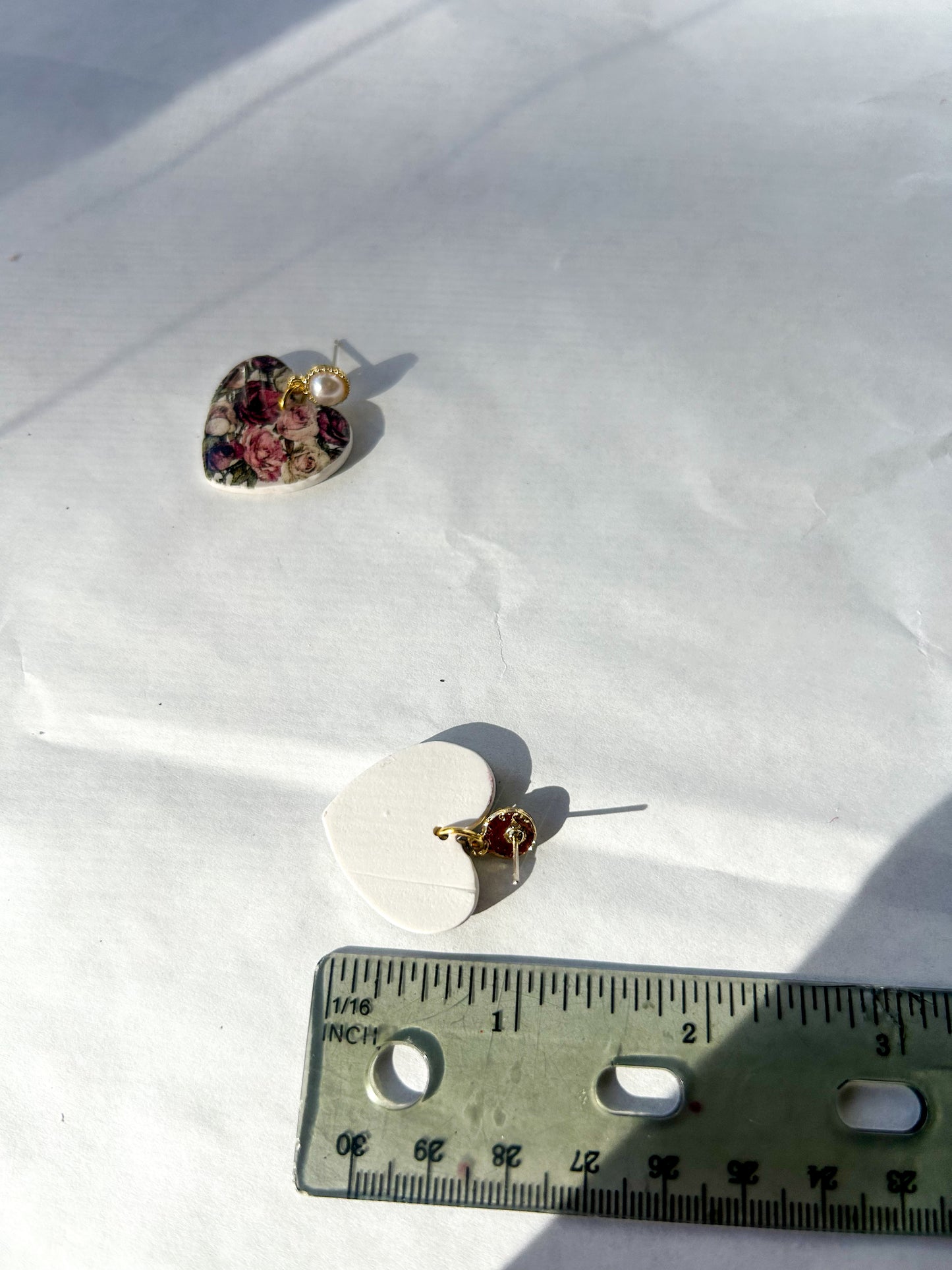 Heart-shaped jewelry pieces on a white surface with a ruler for scale. About an inch in length.