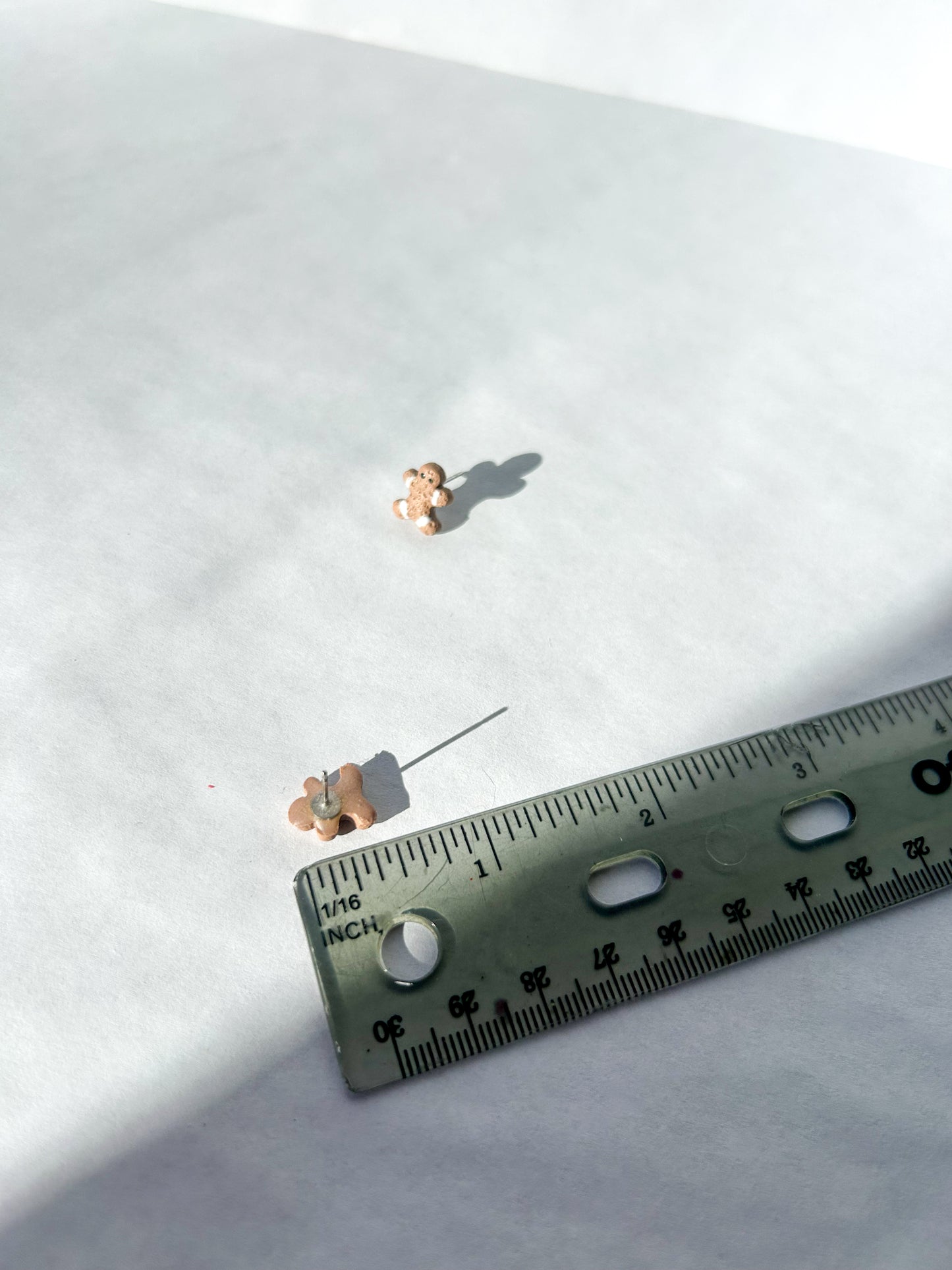 Two small gingerbread man earrings on a white surface with a ruler for scale.