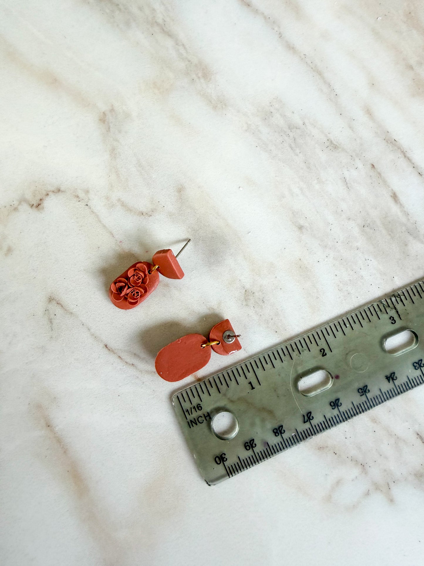 Orange earrings on a marble surface with a ruler for scale. About an inch long