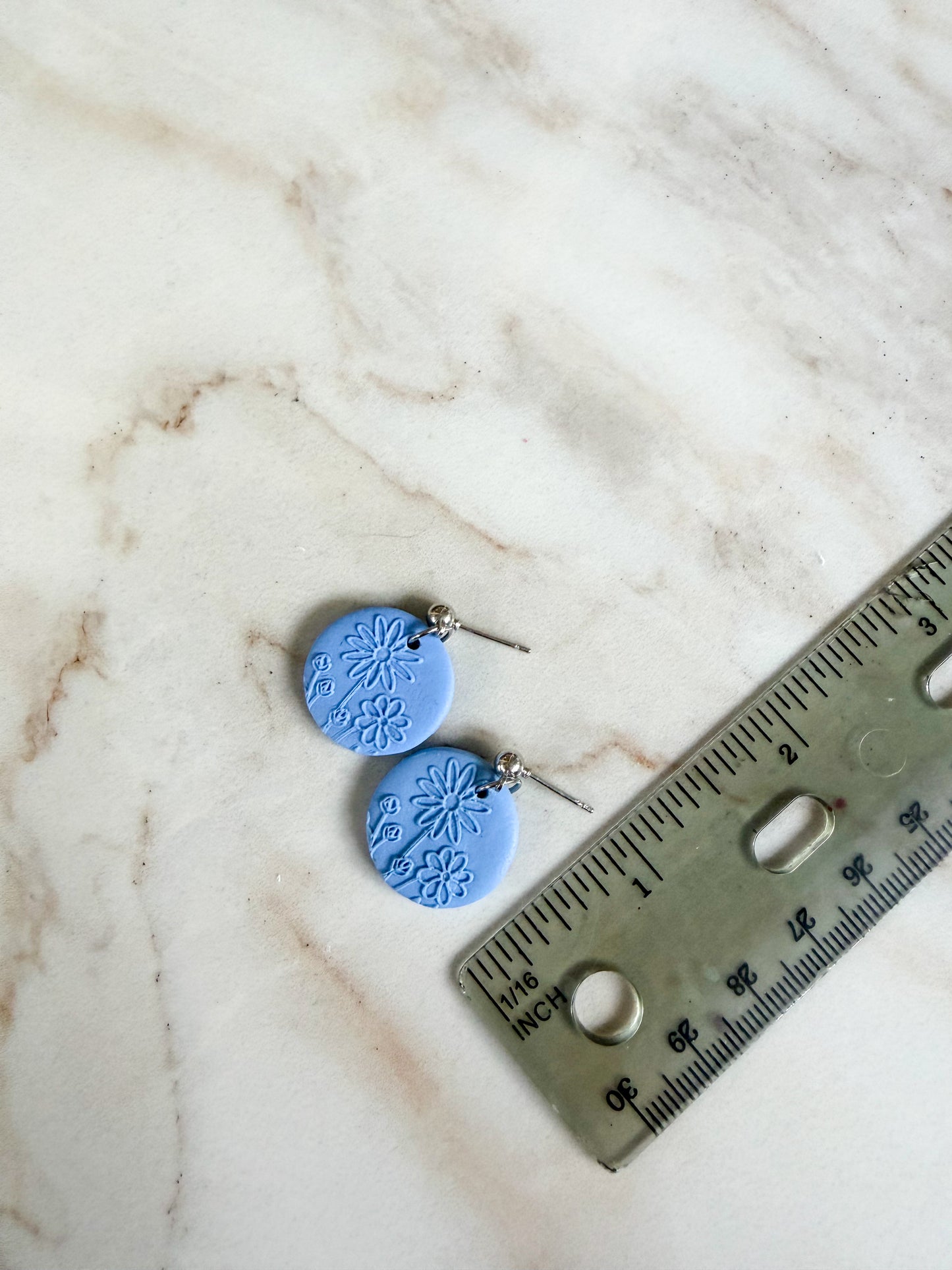Blue ceramic earrings on a marble surface with a ruler for scale. About 1 inch in length