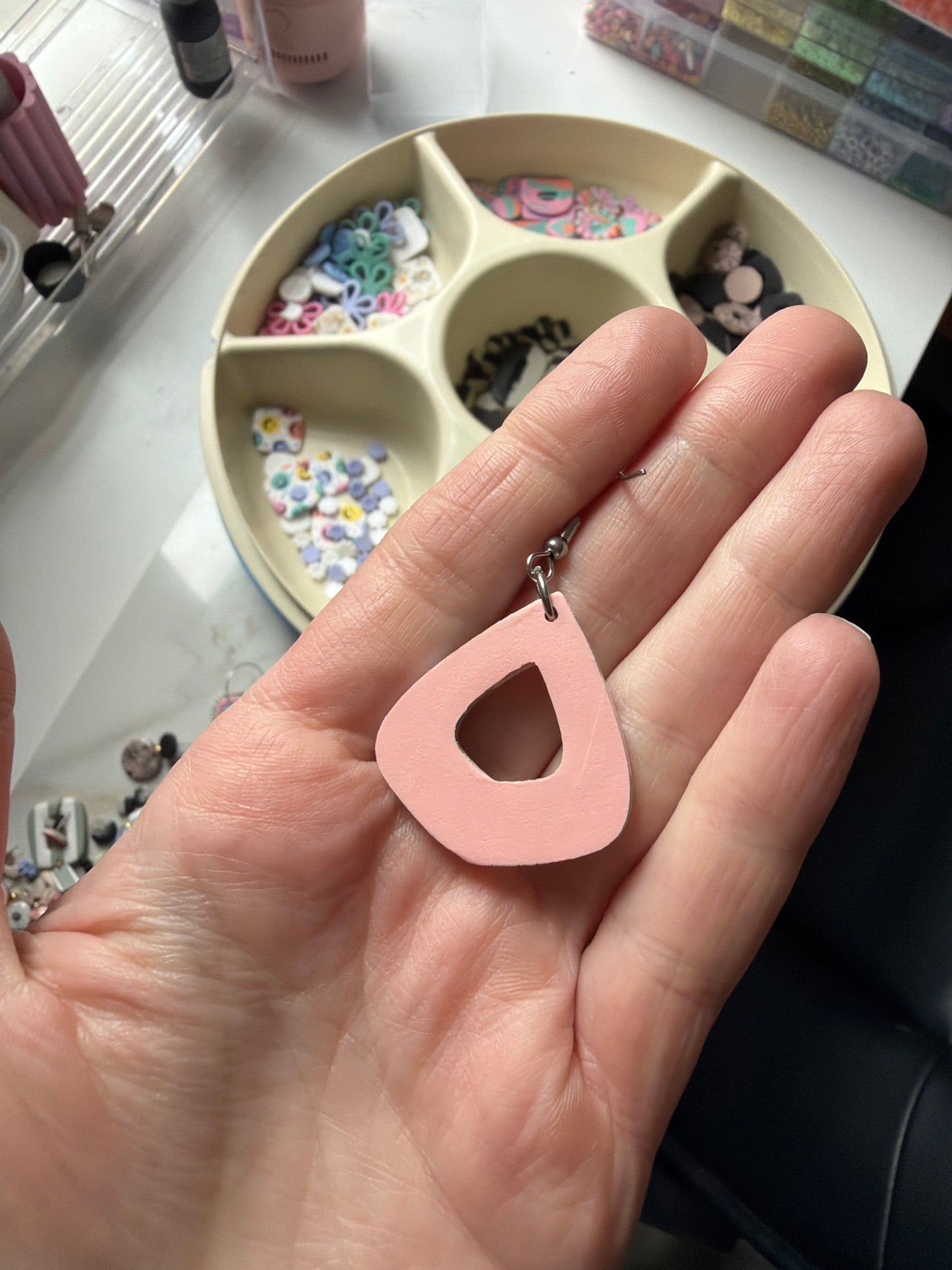 Teardrop shaped earring held in a hand. This picture shows the backside of the earring, which is a coral color.