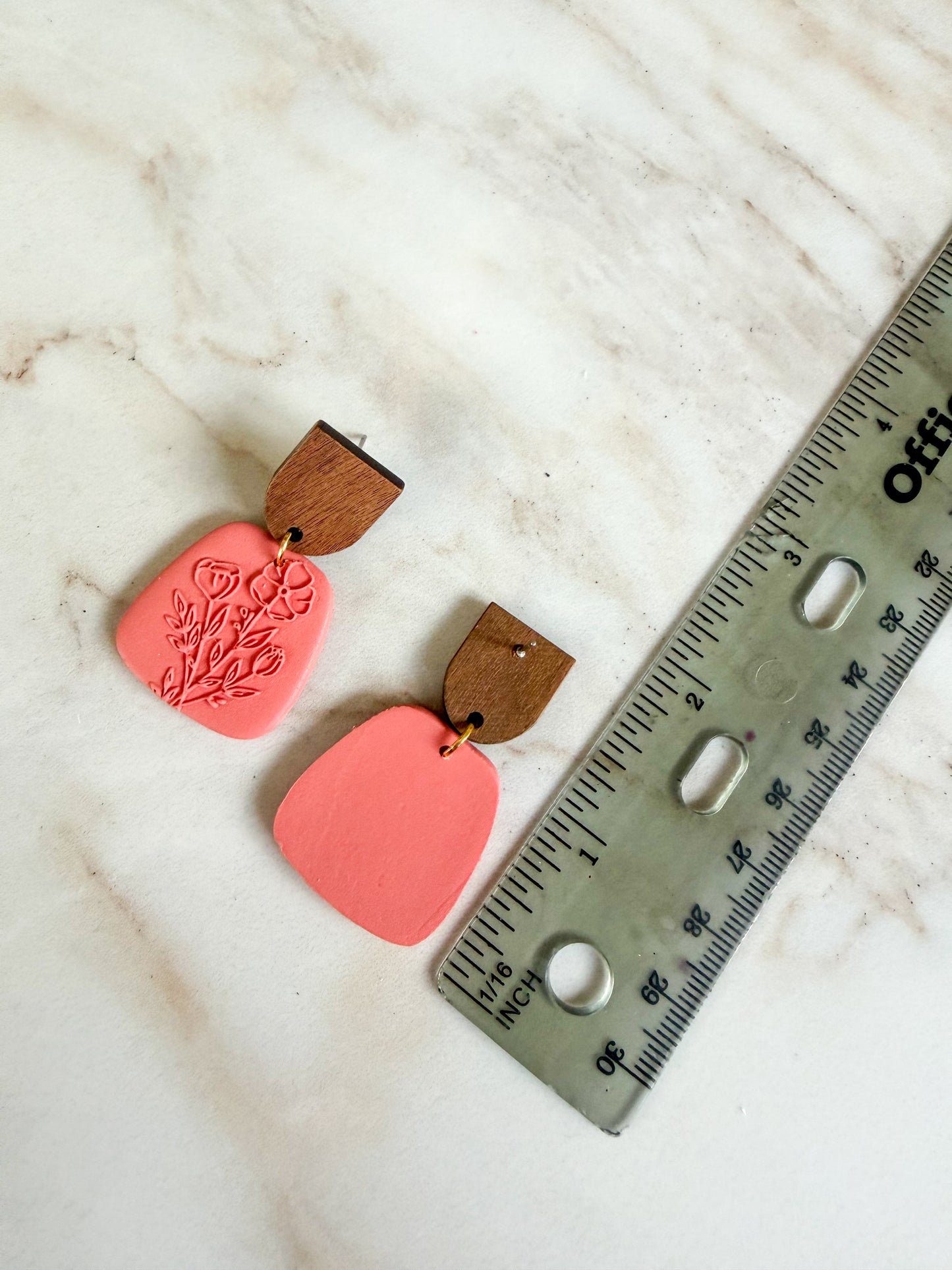 Pink earrings with wooden accents on a marble surface next to a ruler for scale. About 2 inches in length.