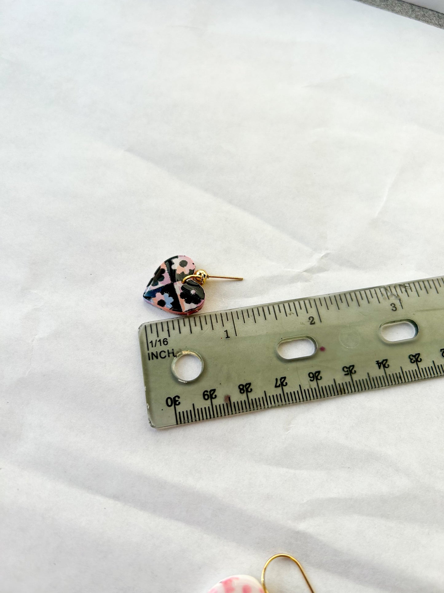 Smaller earring, laying next to a ruler for scale to show that they are about an inch long