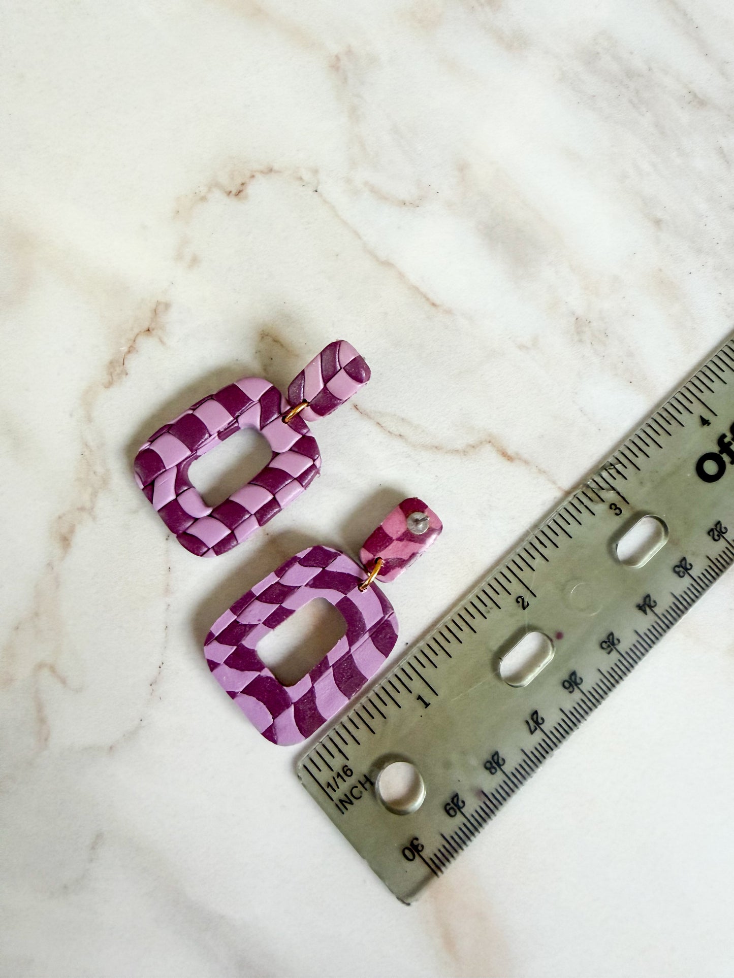 Purple geometric earrings on a marble surface with a ruler for scale. About 2 inches long.