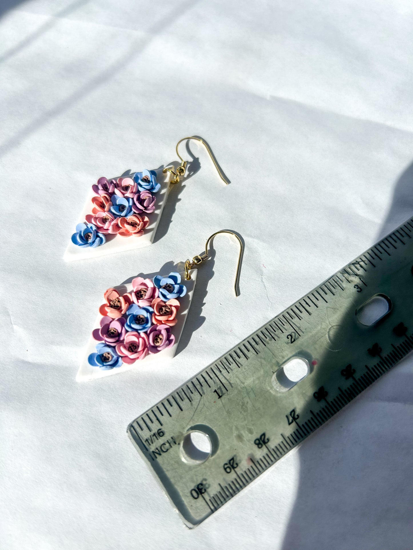 Colorful flower-shaped earrings next to a ruler on a white background. About 2 inches in length.