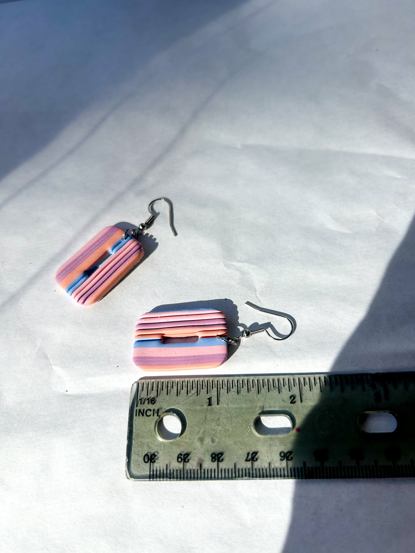 Colorful striped earrings on a white surface with a ruler for scale. 2 inches in length.
