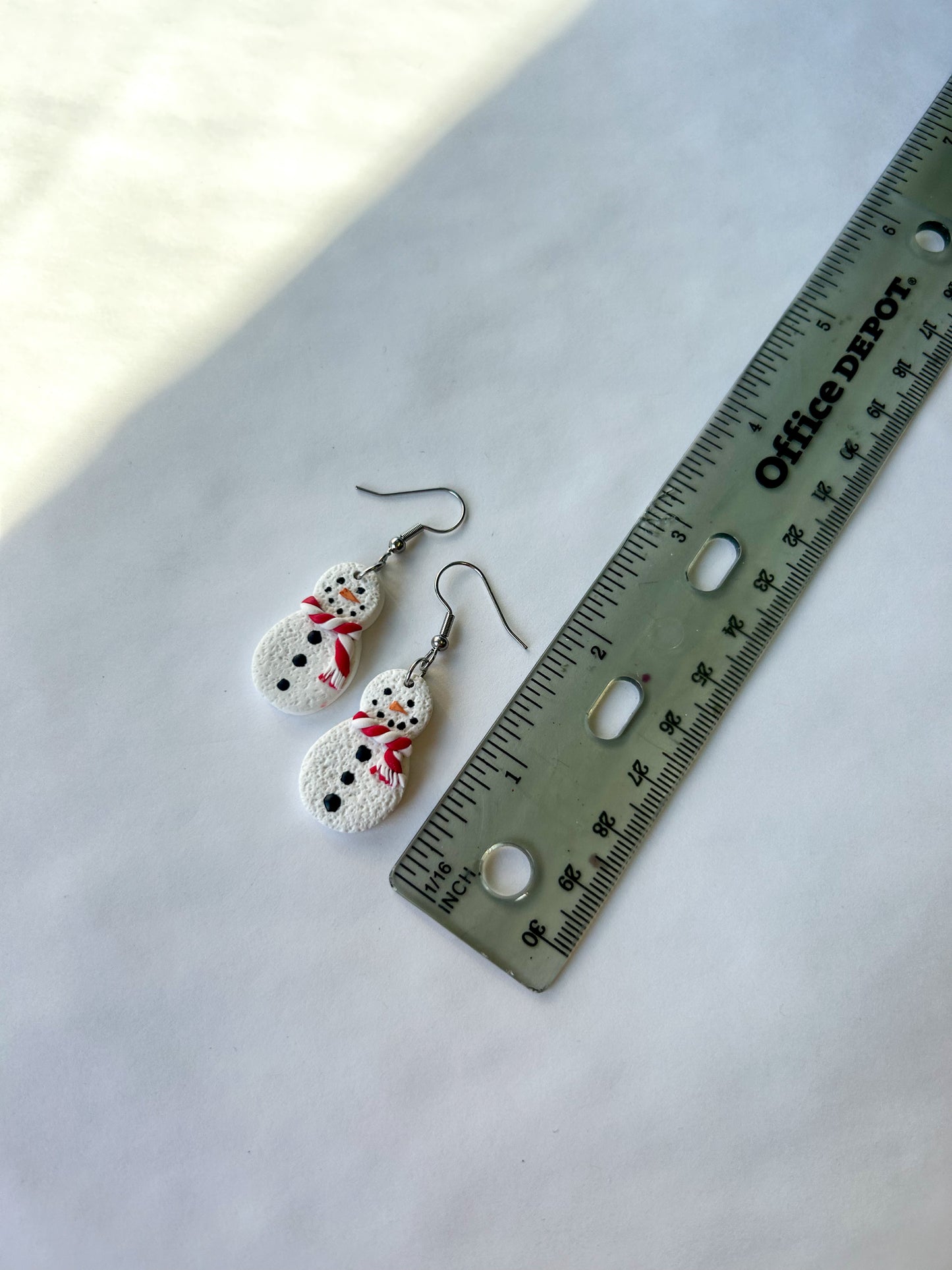 Pair of snowman-shaped earrings next to a ruler on a white background