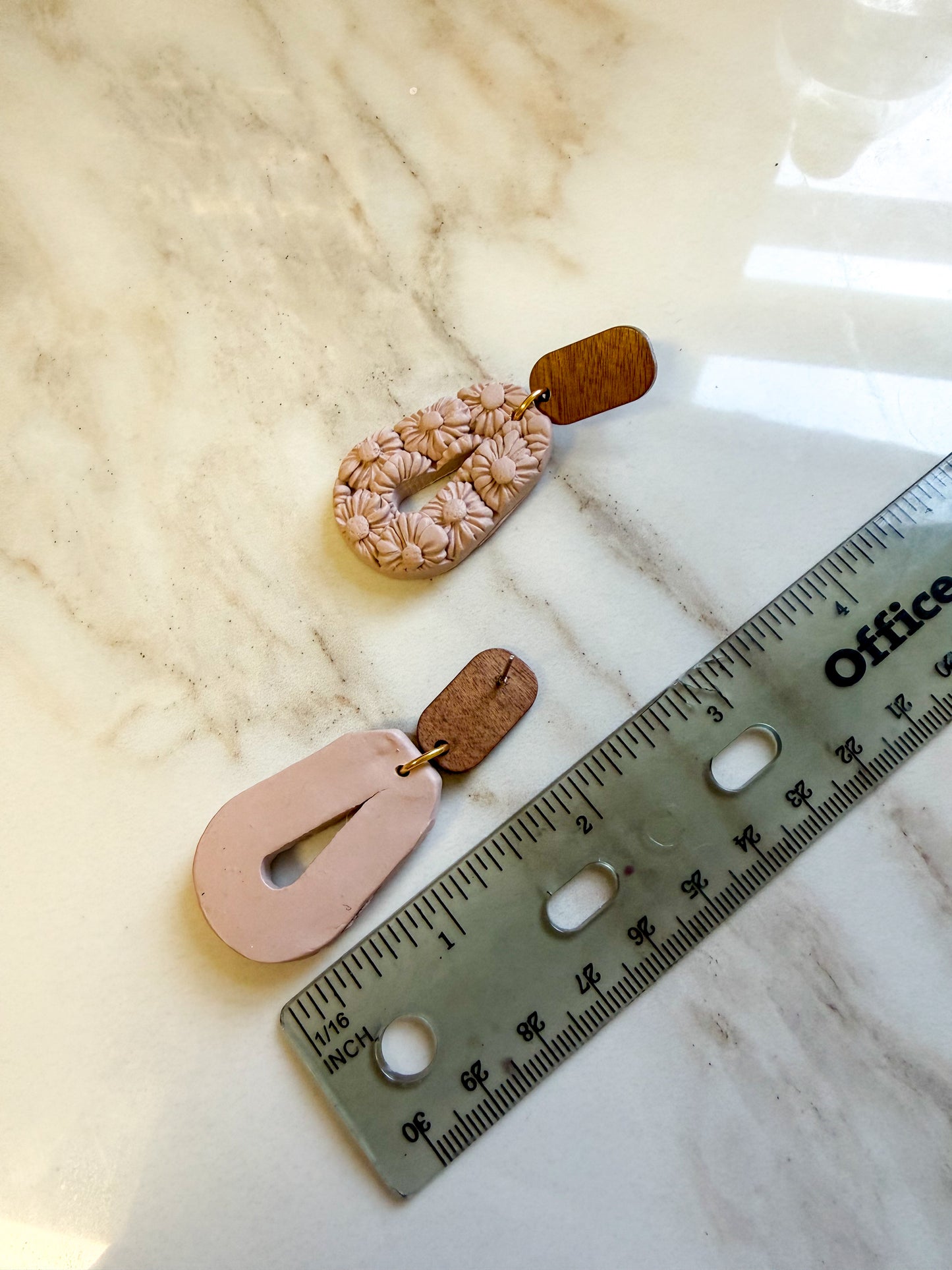 Earrings laying next to a ruler for scale. Approximately 2.5 inches in length. The earrings have textured flowers covering the surface.