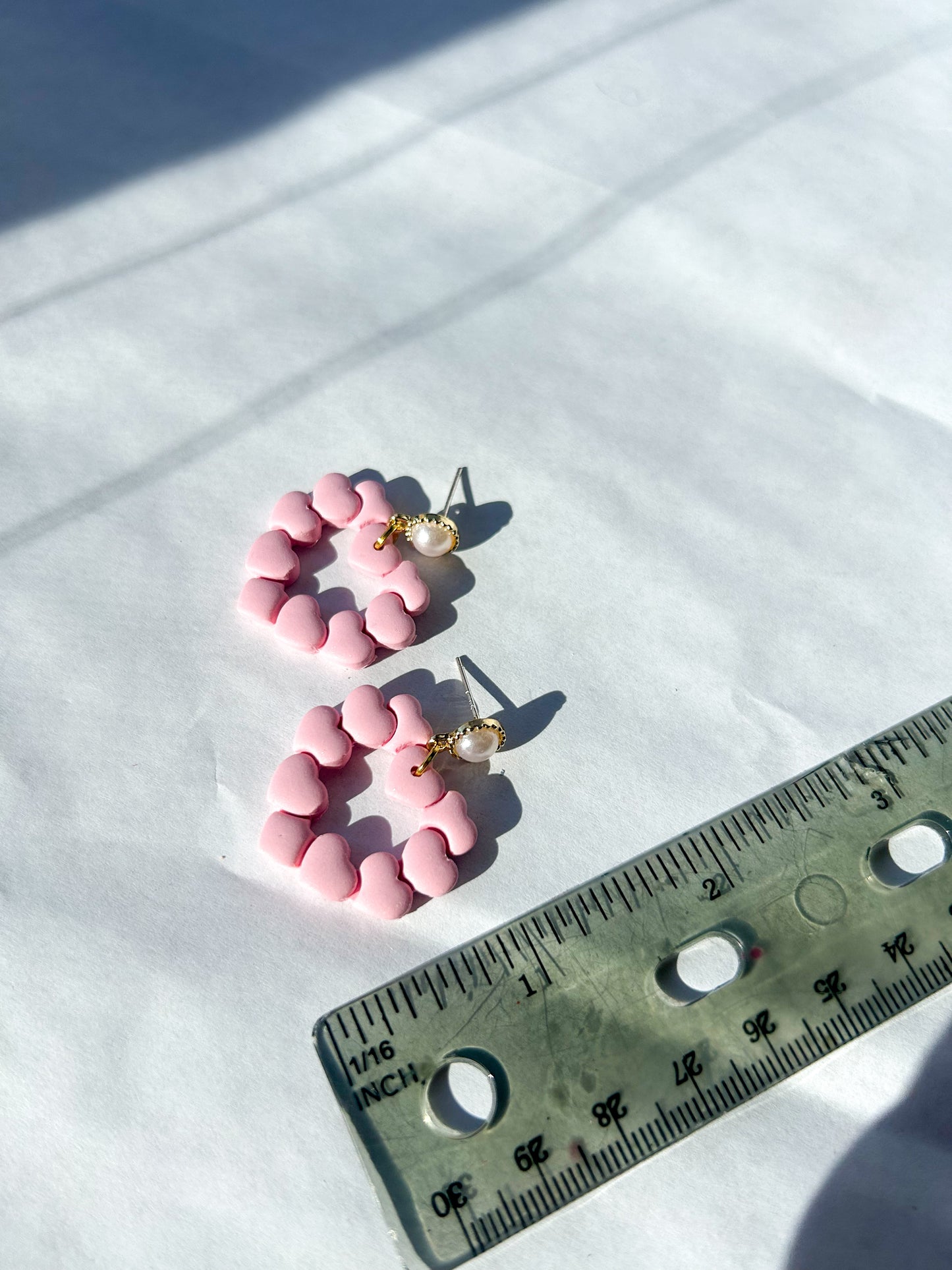 Pink earrings on a white surface with a ruler for scale. About 2.25 inches