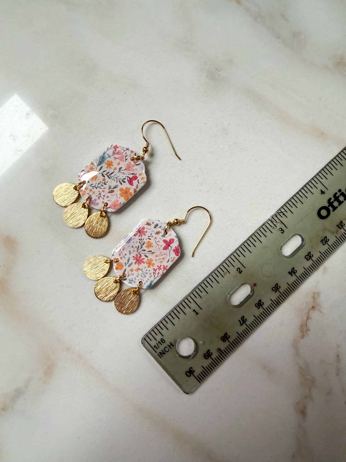 Floral earrings with gold accents on a marble surface with a ruler for scale. About 2.5 inches long.