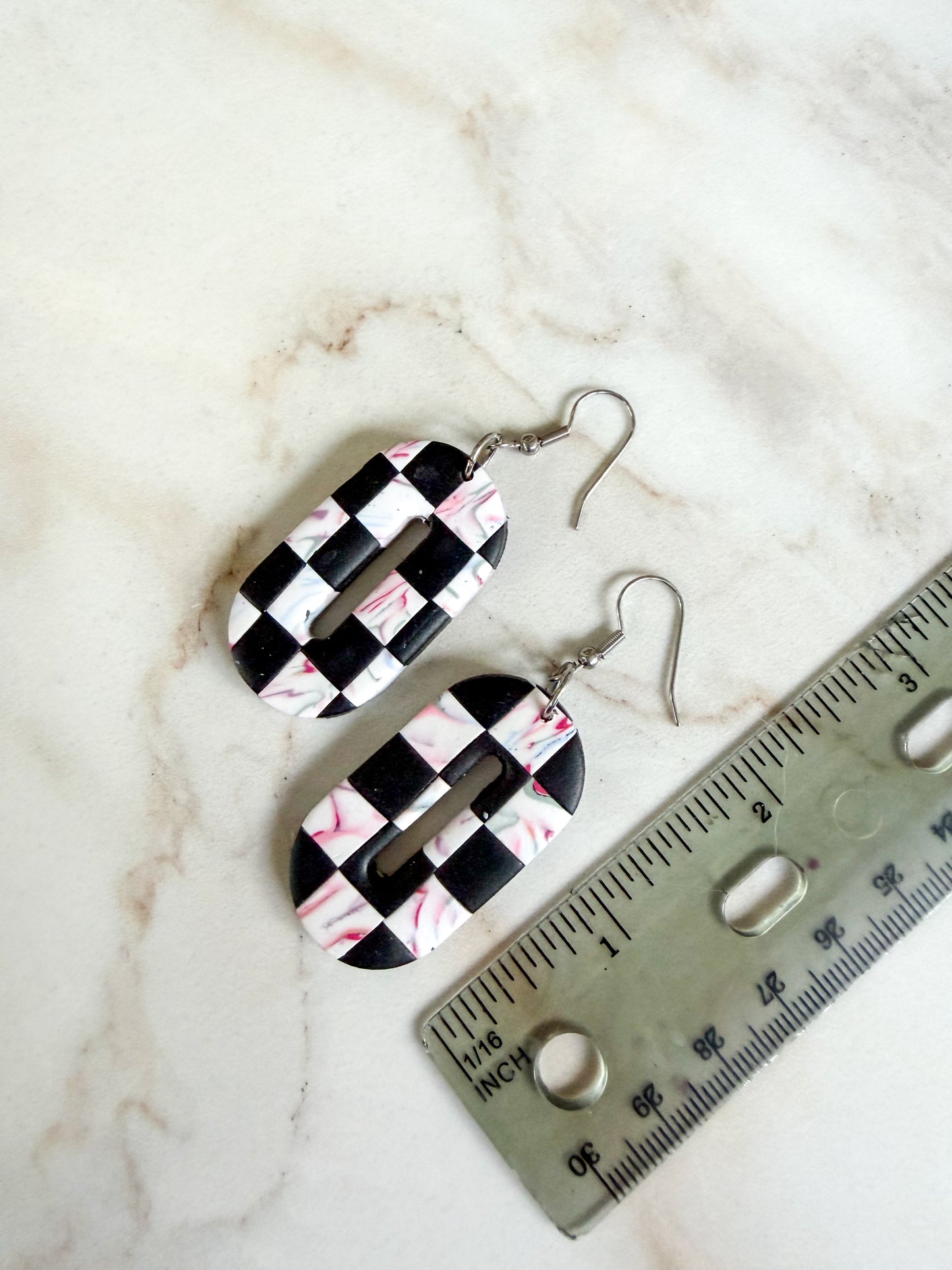 Black and white checkered earrings on a marble surface with a ruler for scale. About 2 inches long.