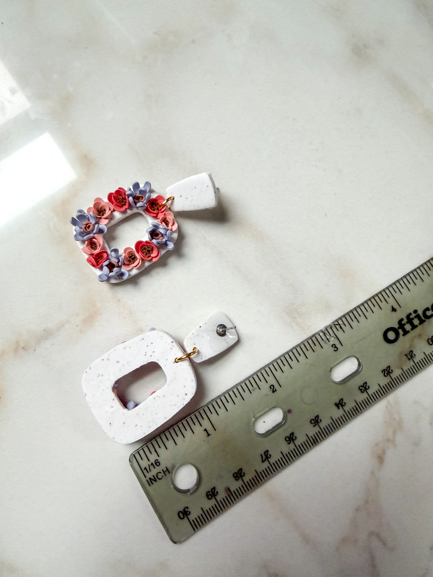 Floral earrings on a marble surface with a ruler for scale. About 2 inches long.