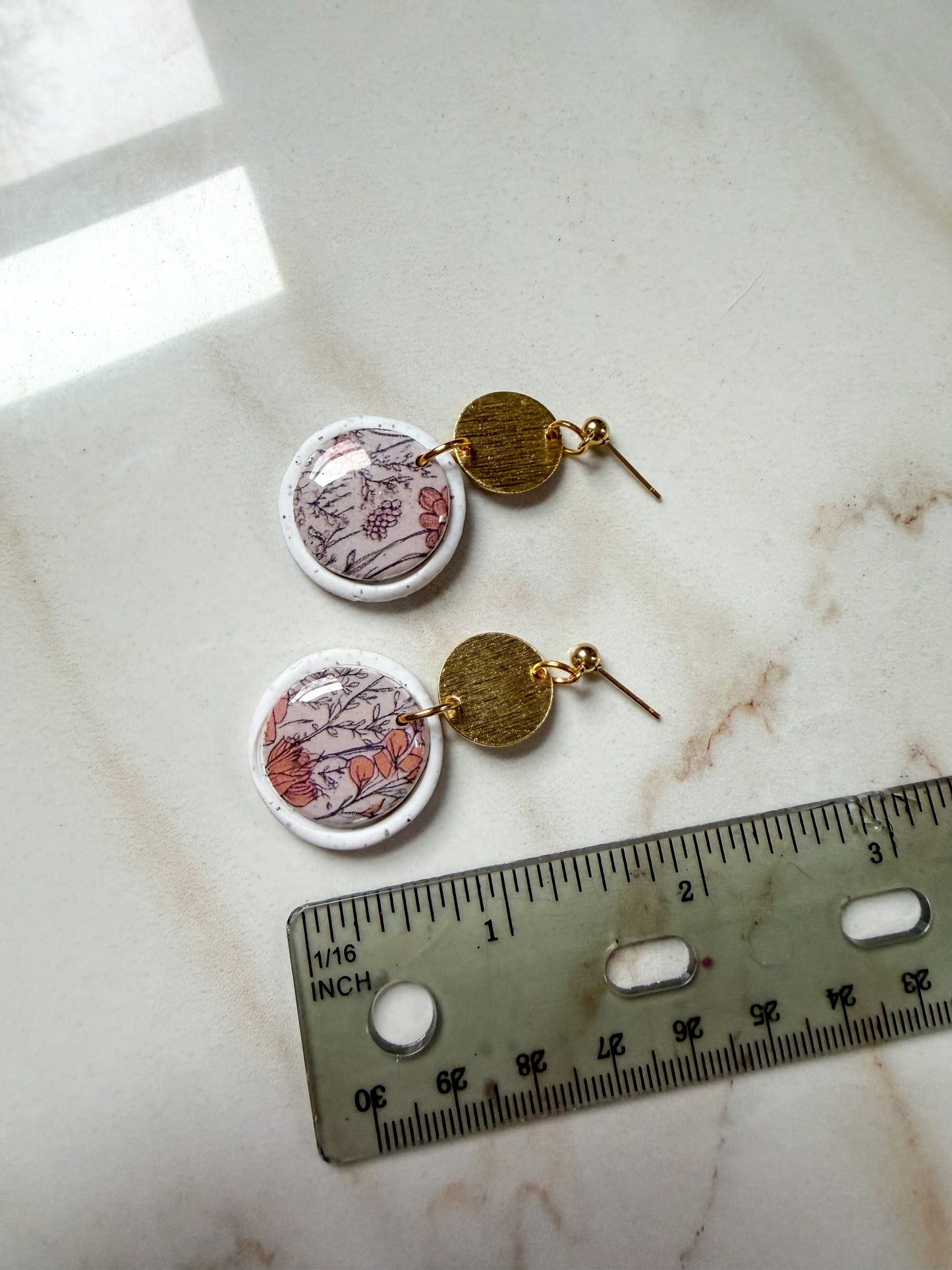 Pair of earrings with floral design on a marble surface with a ruler for scale. A little under 2 inches long.