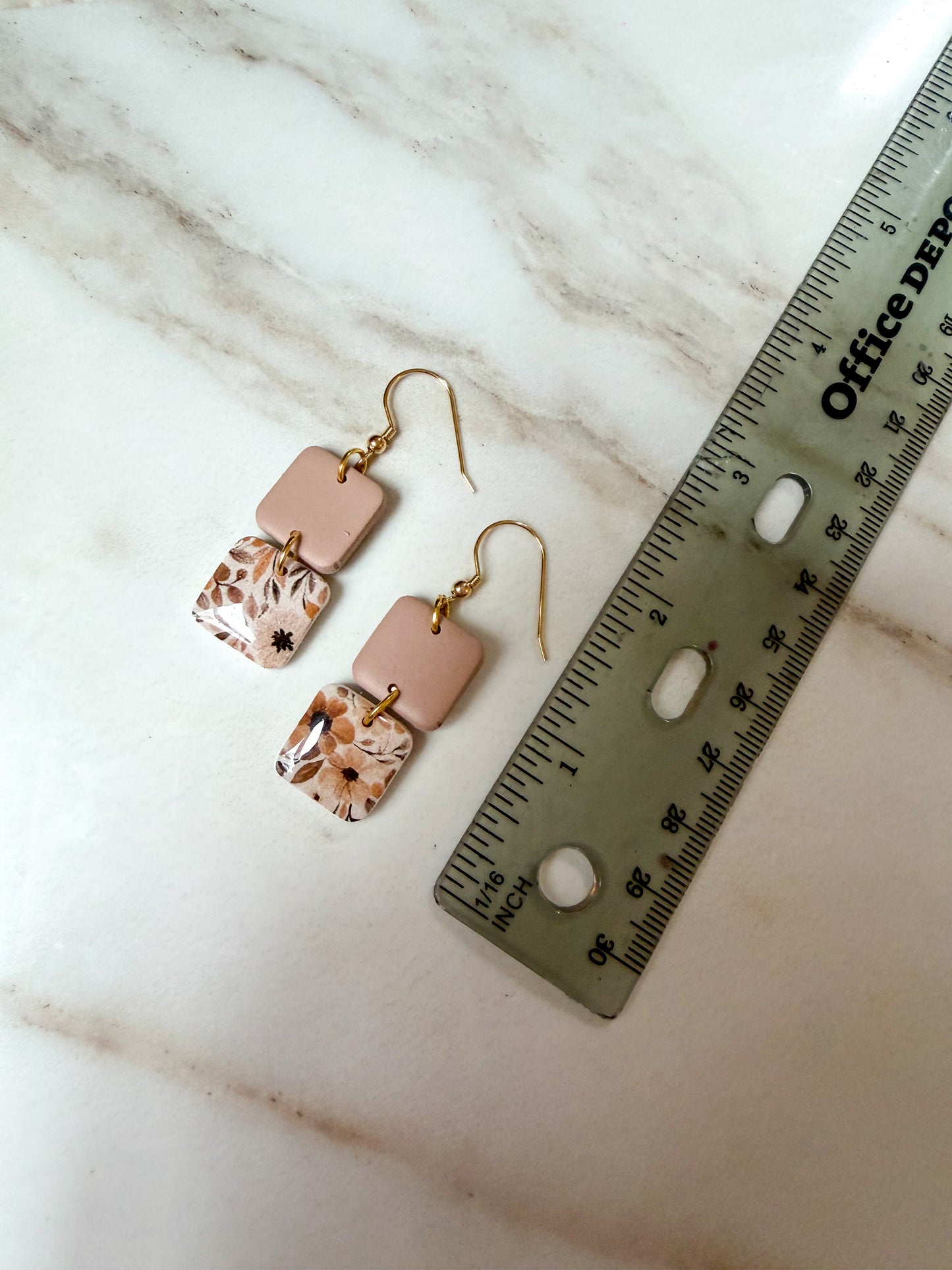 A pair of dangling earrings with rectangular blush pink and marbled beige-and-brown charms, shown next to a ruler on a white marble surface. About 2 inches long.