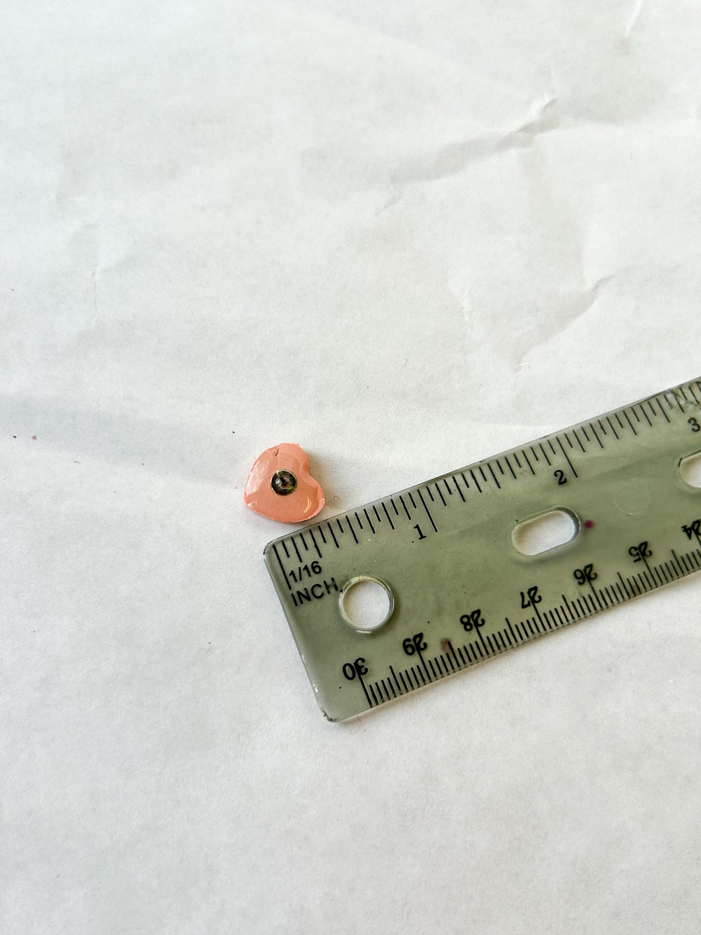 Small pink heart-shaped object next to a ruler on a white background
Half an inch length