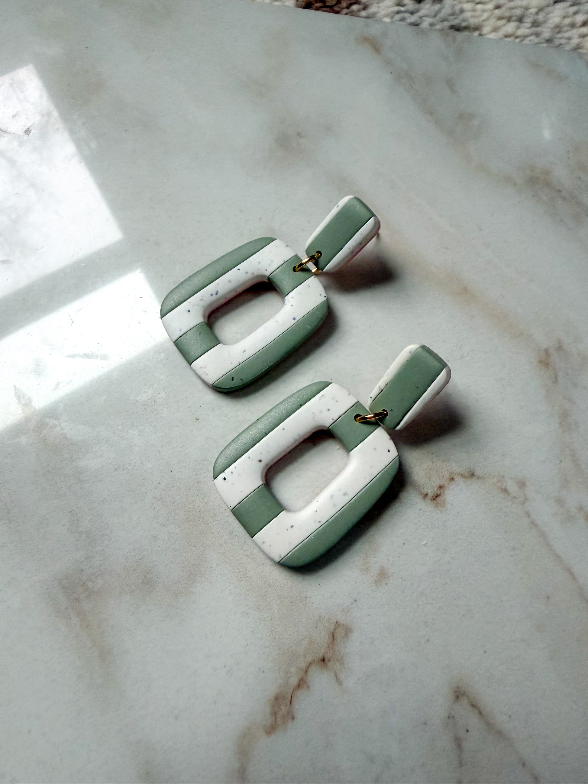 Green and white earrings on a marble surface