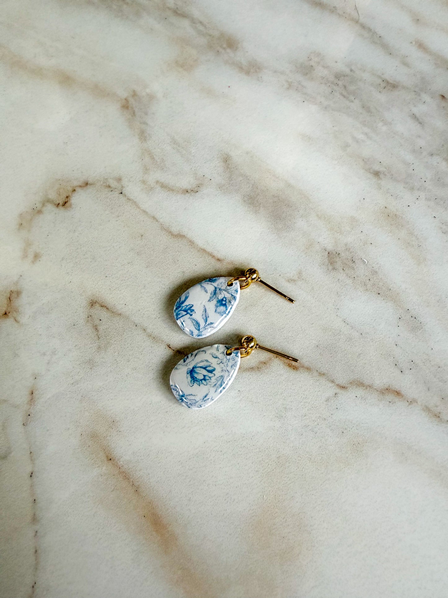Teardrop-shaped earrings with blue floral pattern on a marble surface