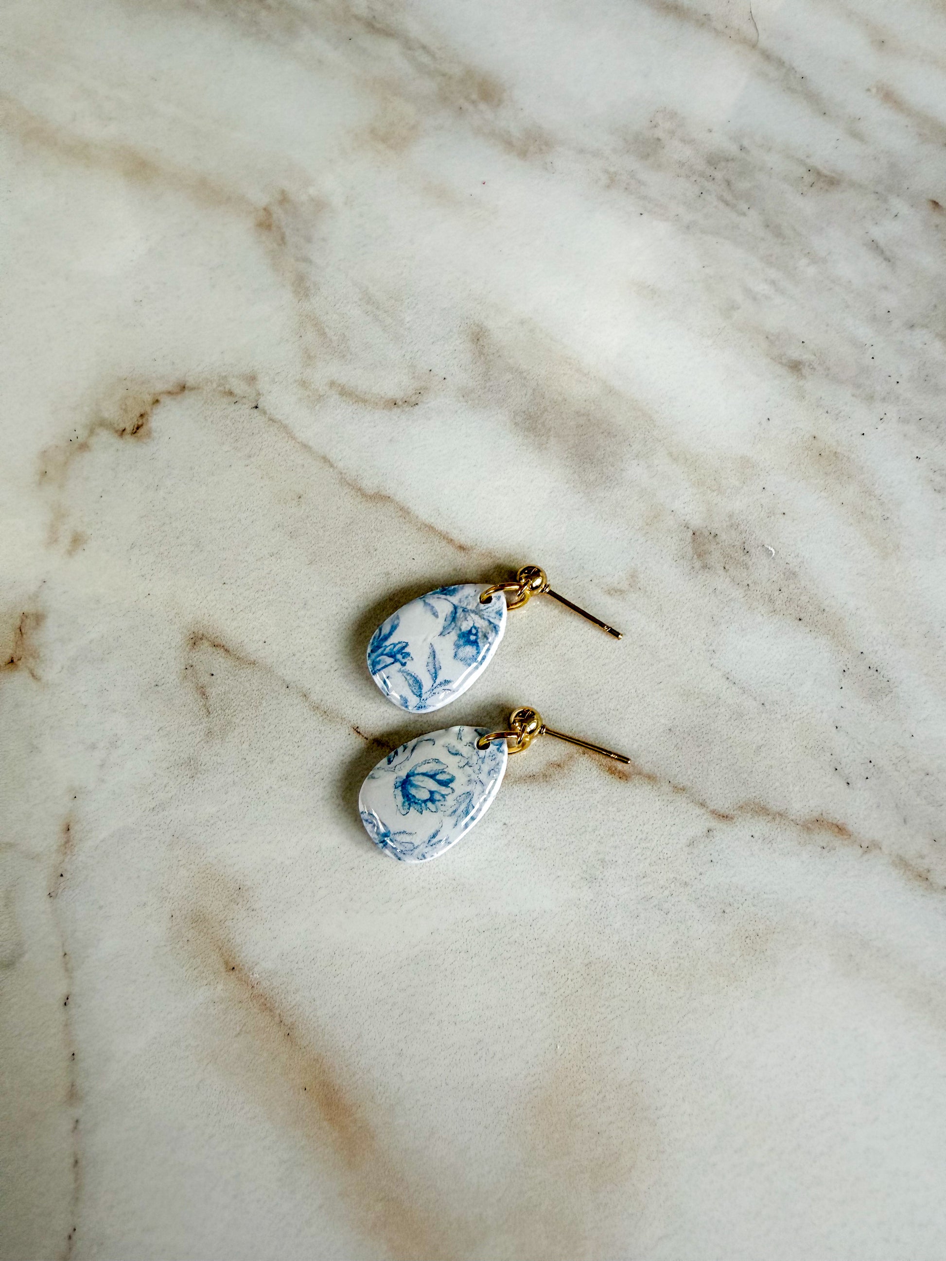 Teardrop-shaped earrings with blue floral pattern on a marble surface