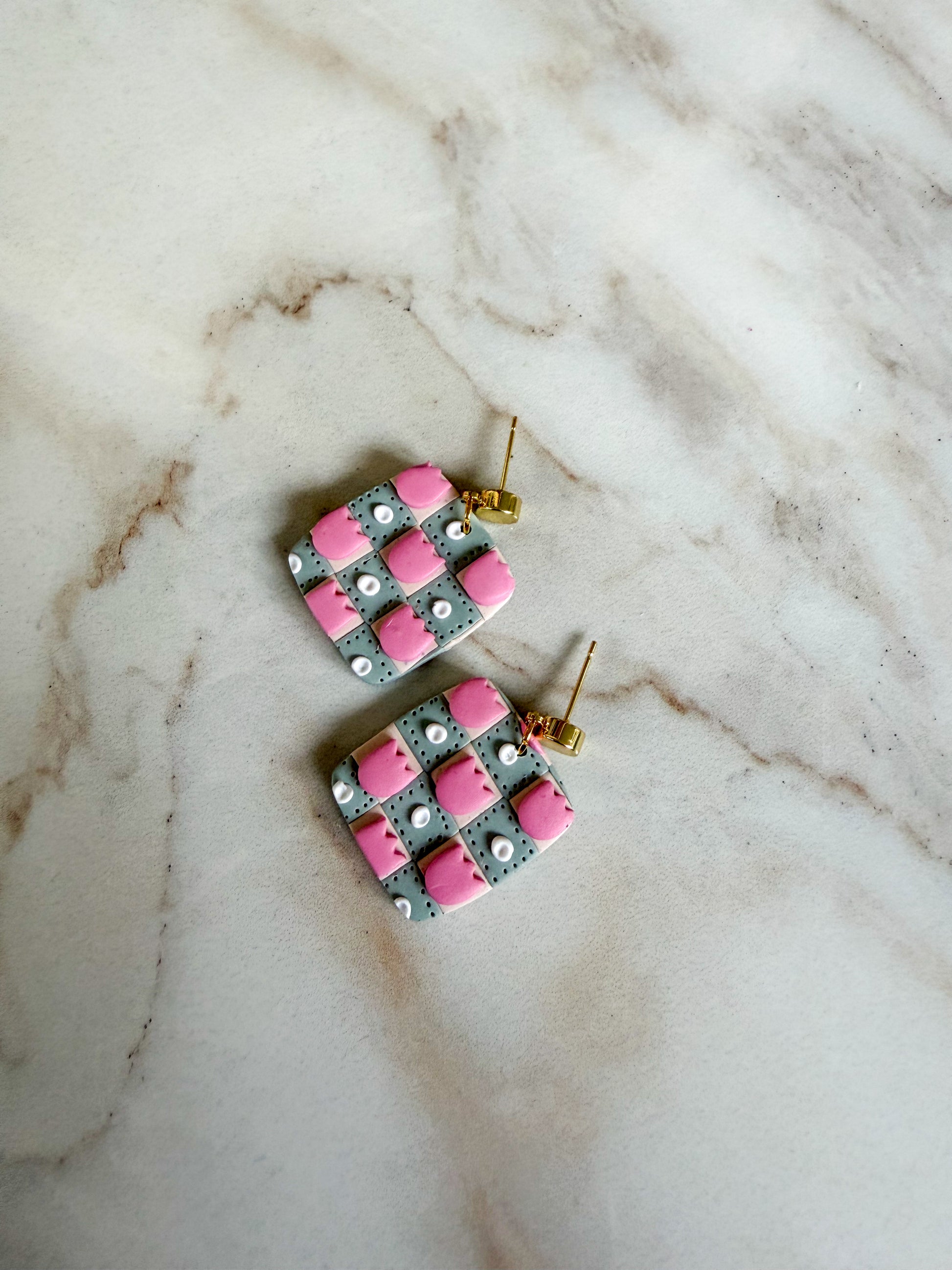 Pair of earrings with pink and gray pattern on a marble surface