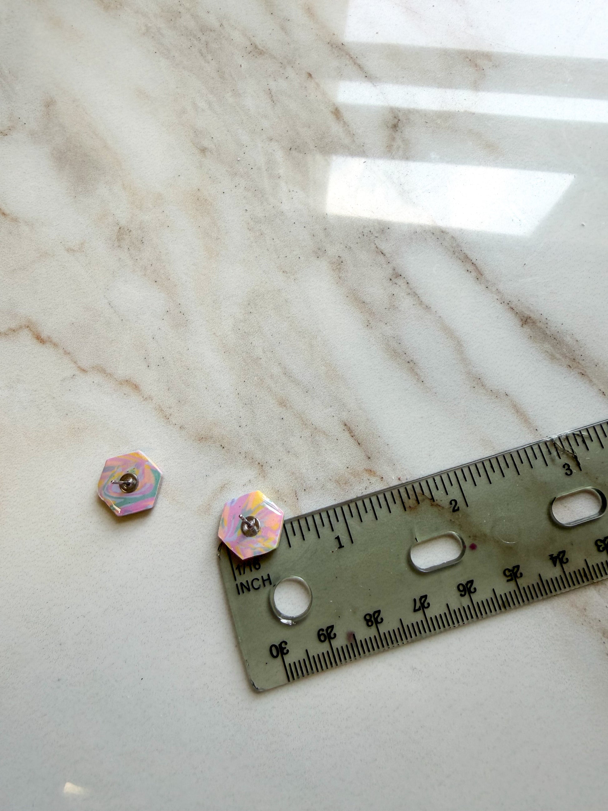Two small hexagonal studs shown on a light marble surface next to a ruler for scale. About 1/2 inch in length. 