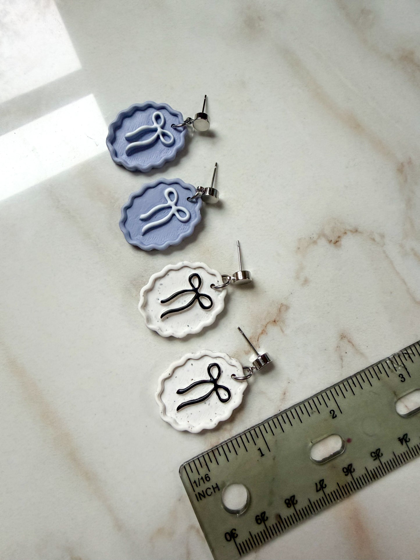 Set of earrings with decorative elements on a marble surface with a ruler for scale. About an inch and a half long. 