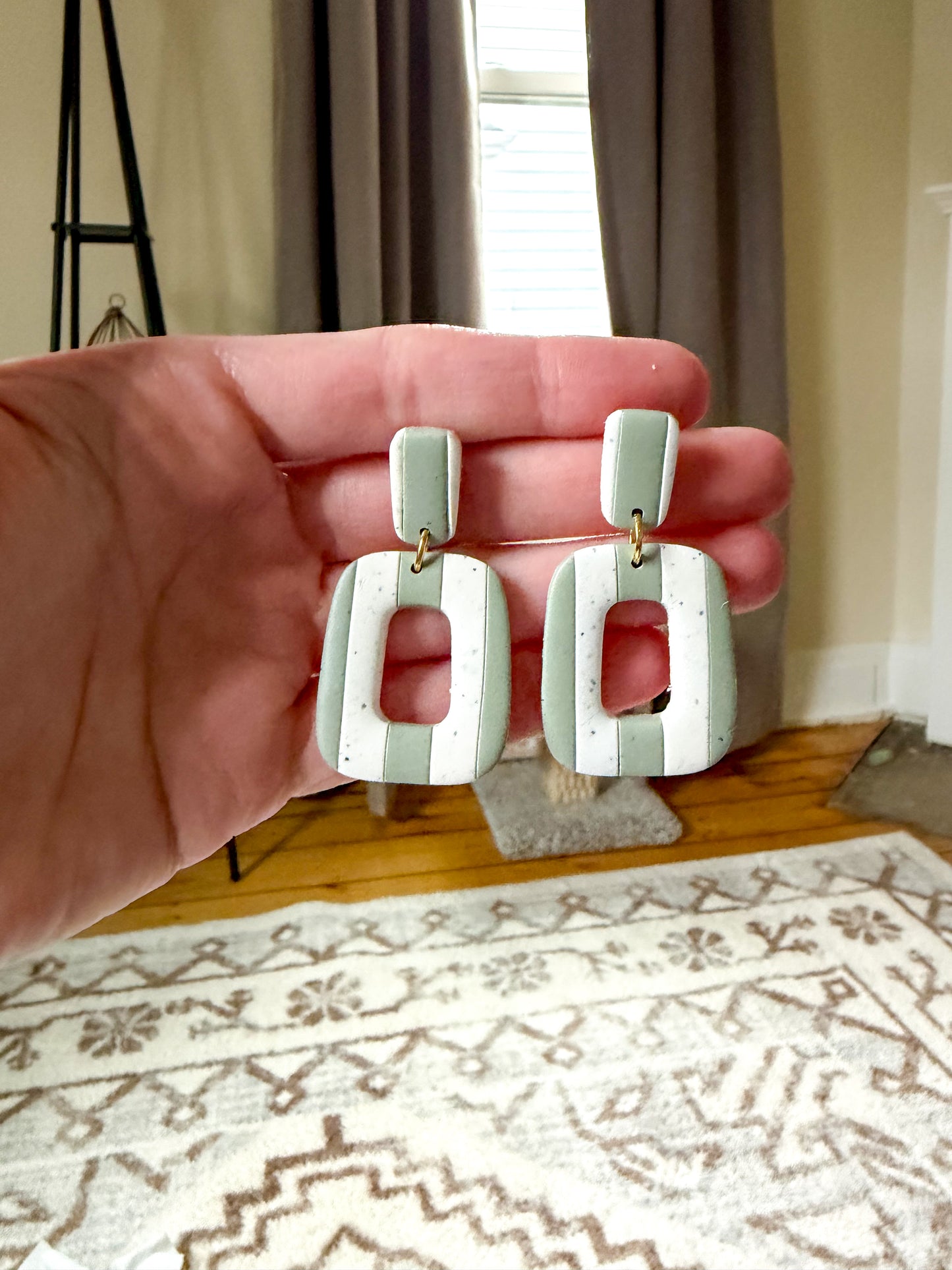 Hand holding a pair of light green earrings with a neutral background