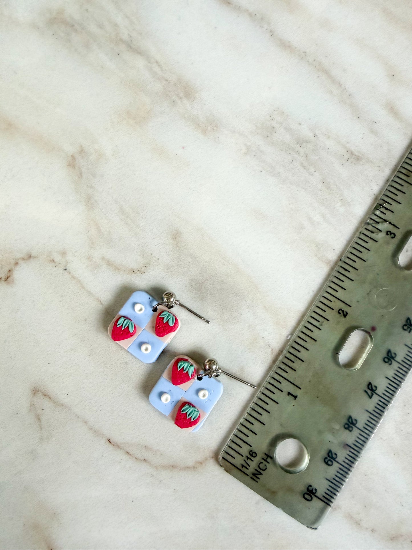 Pair of strawberry-themed earrings on a marble surface with a ruler for scale. About an inch in length 