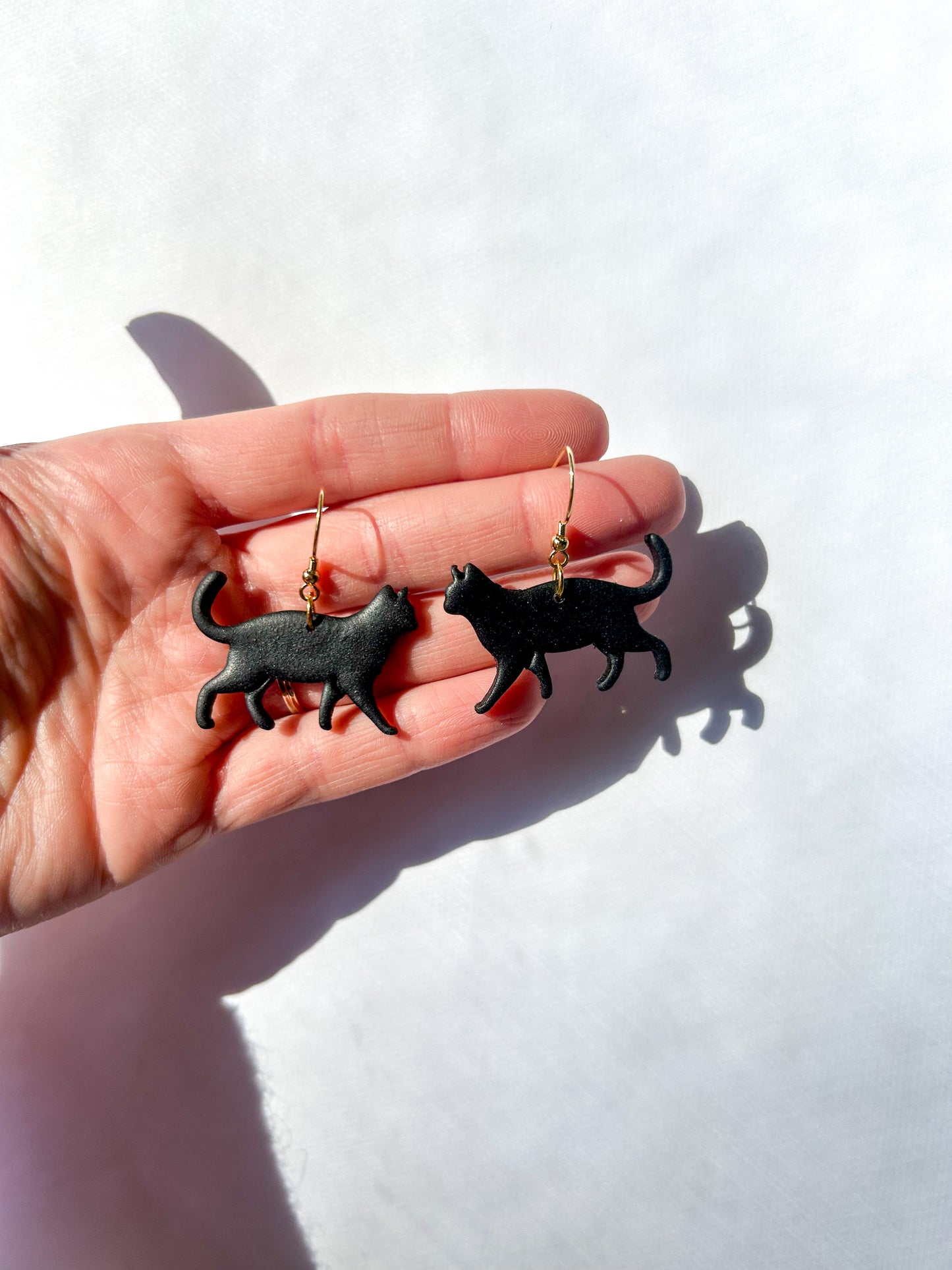 Black cat-shaped earrings held in a hand against a white background