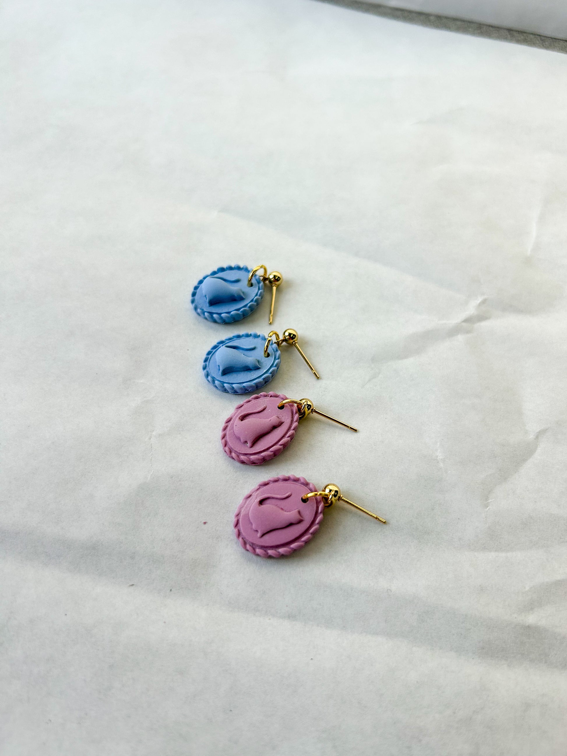 two pairs of earrings with scalloped borders and cats in the center. Laying on a flat surface
