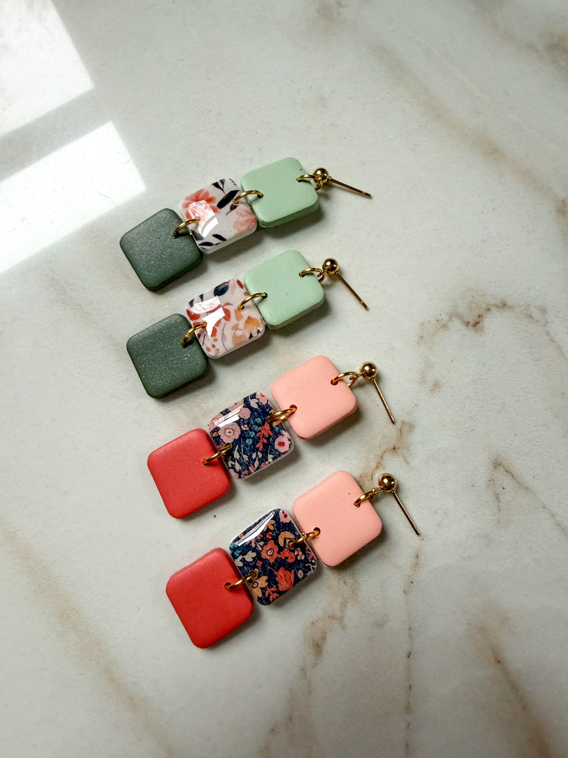 Two pairs of colorful square earrings on a marble surface