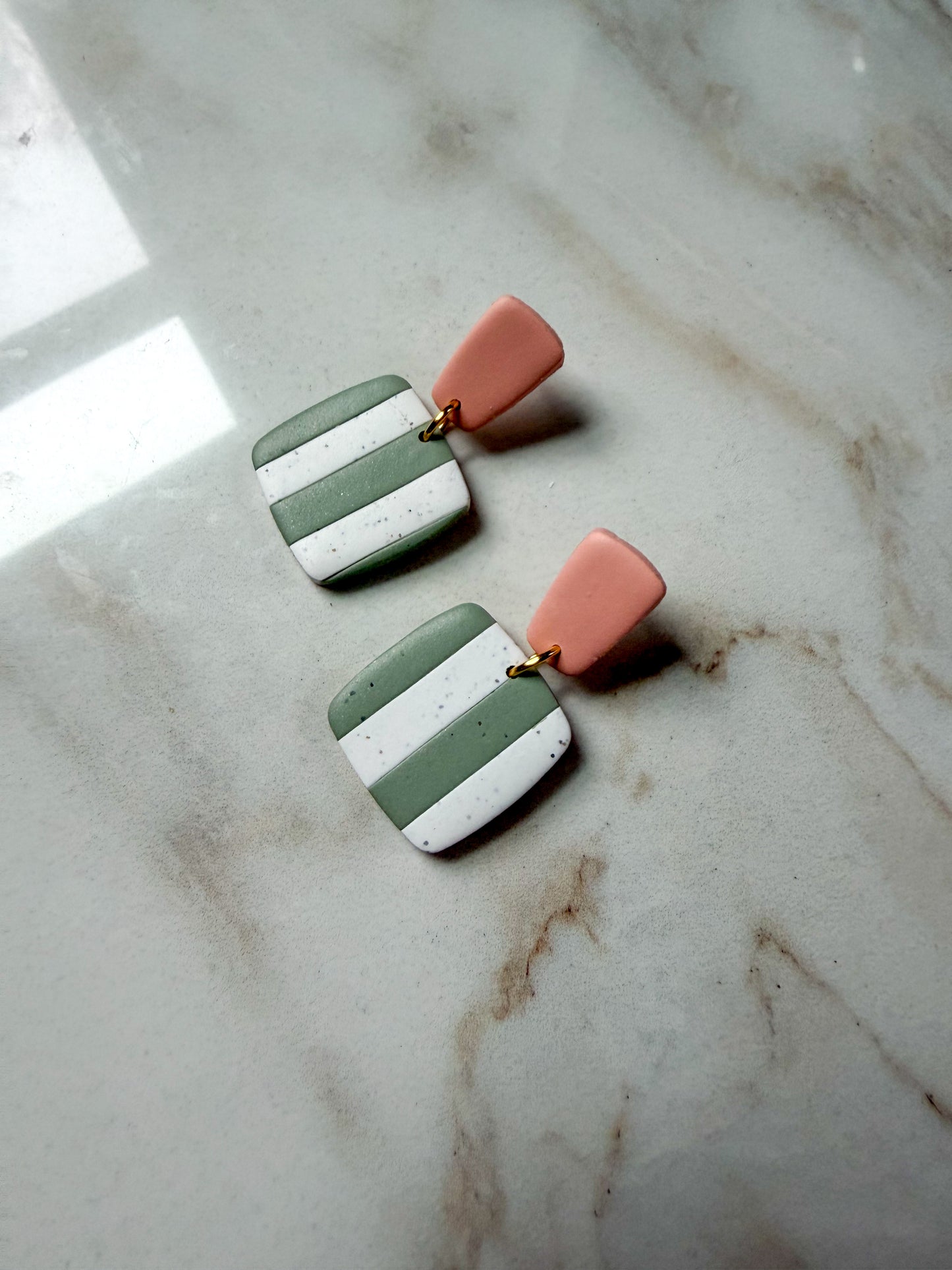 Pair of earrings with green and white striped design with pink posts on a marble surface