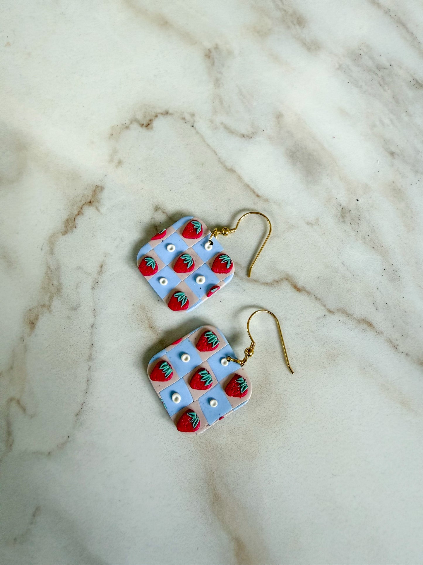 Pair of earrings with strawberry pattern on a marble surface