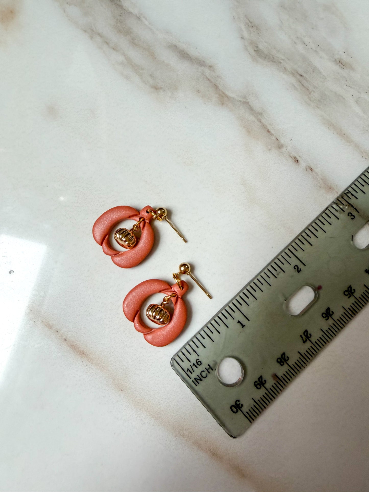 A pair of pumpkin charm earrings next to a ruler for scale. About one inch long. 