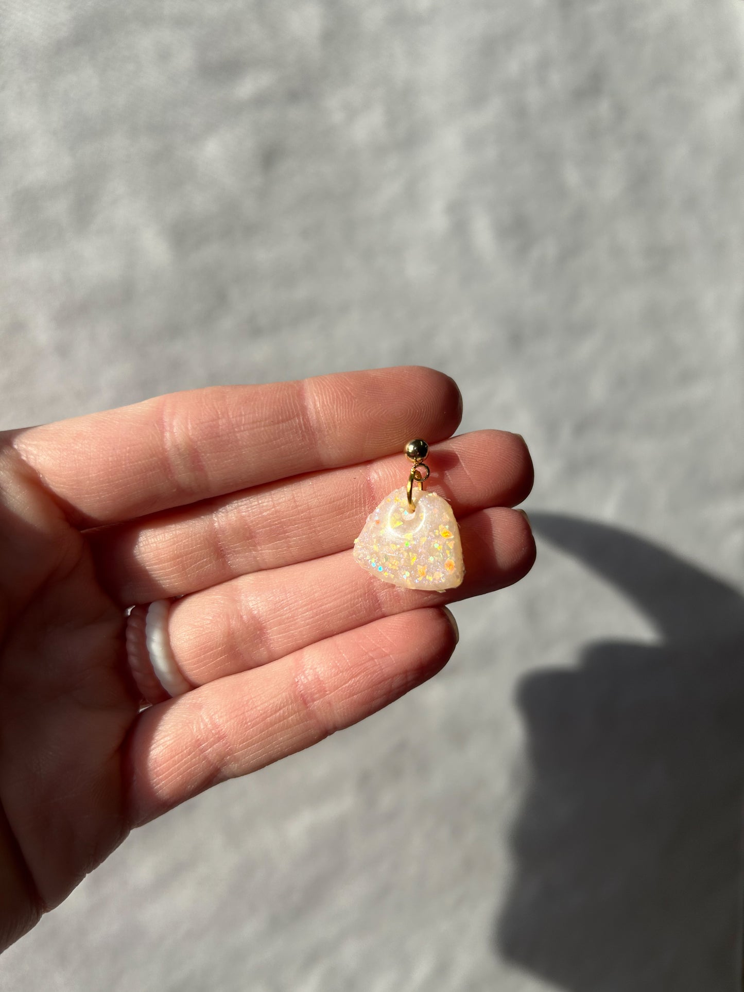 Hand holding a small opal pendant against a neutral background