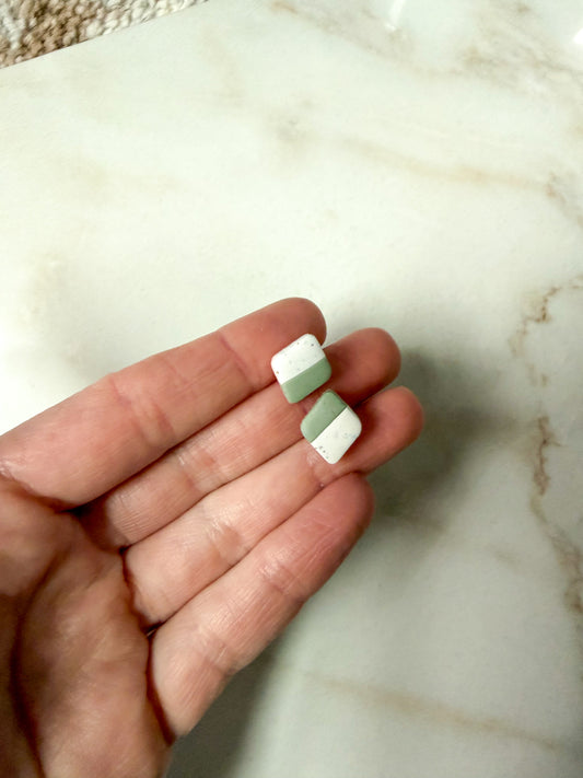 Green and white earrings held in a hand