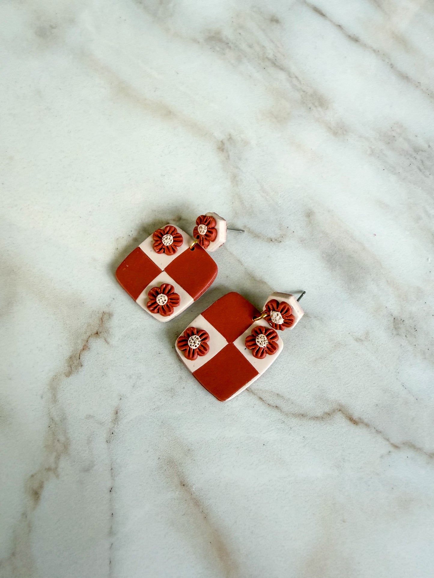 Pair of terracotta and white checkered earrings with floral designs on a marble surface