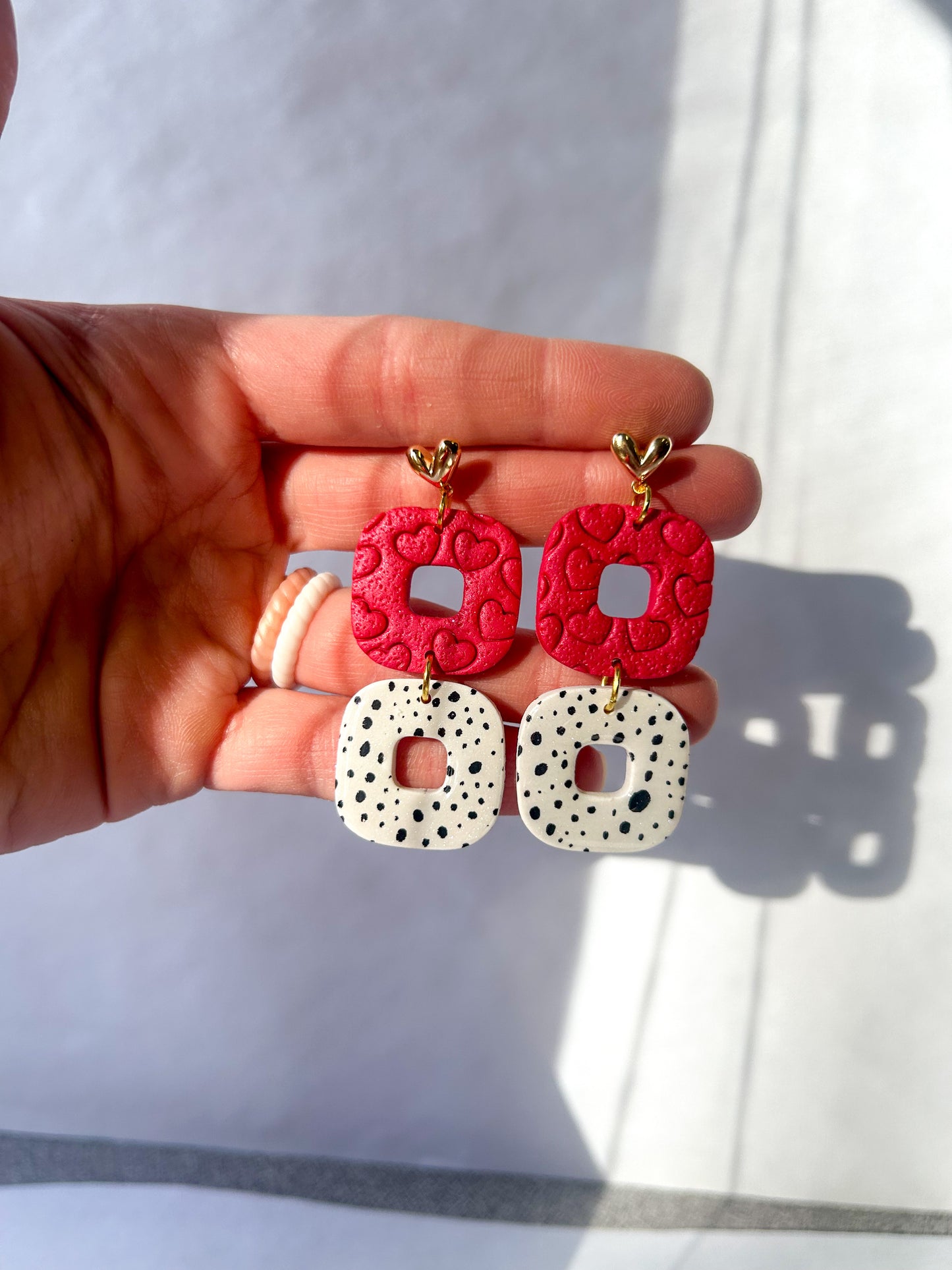 Hand holding red and white patterned earrings against a light background