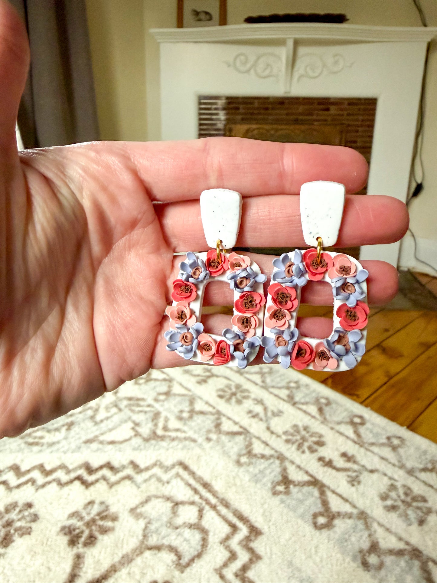 Hand holding floral earrings with a neutral background
