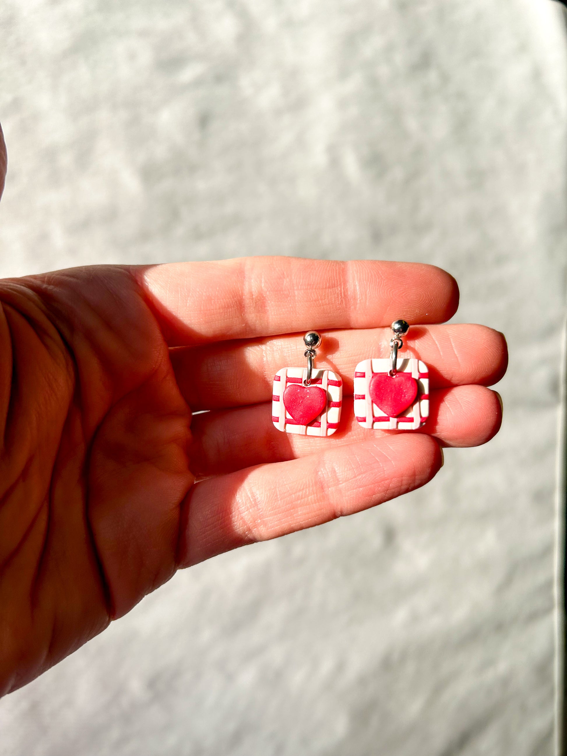 Hand holding a pair of square dangles with 
hearts in the center