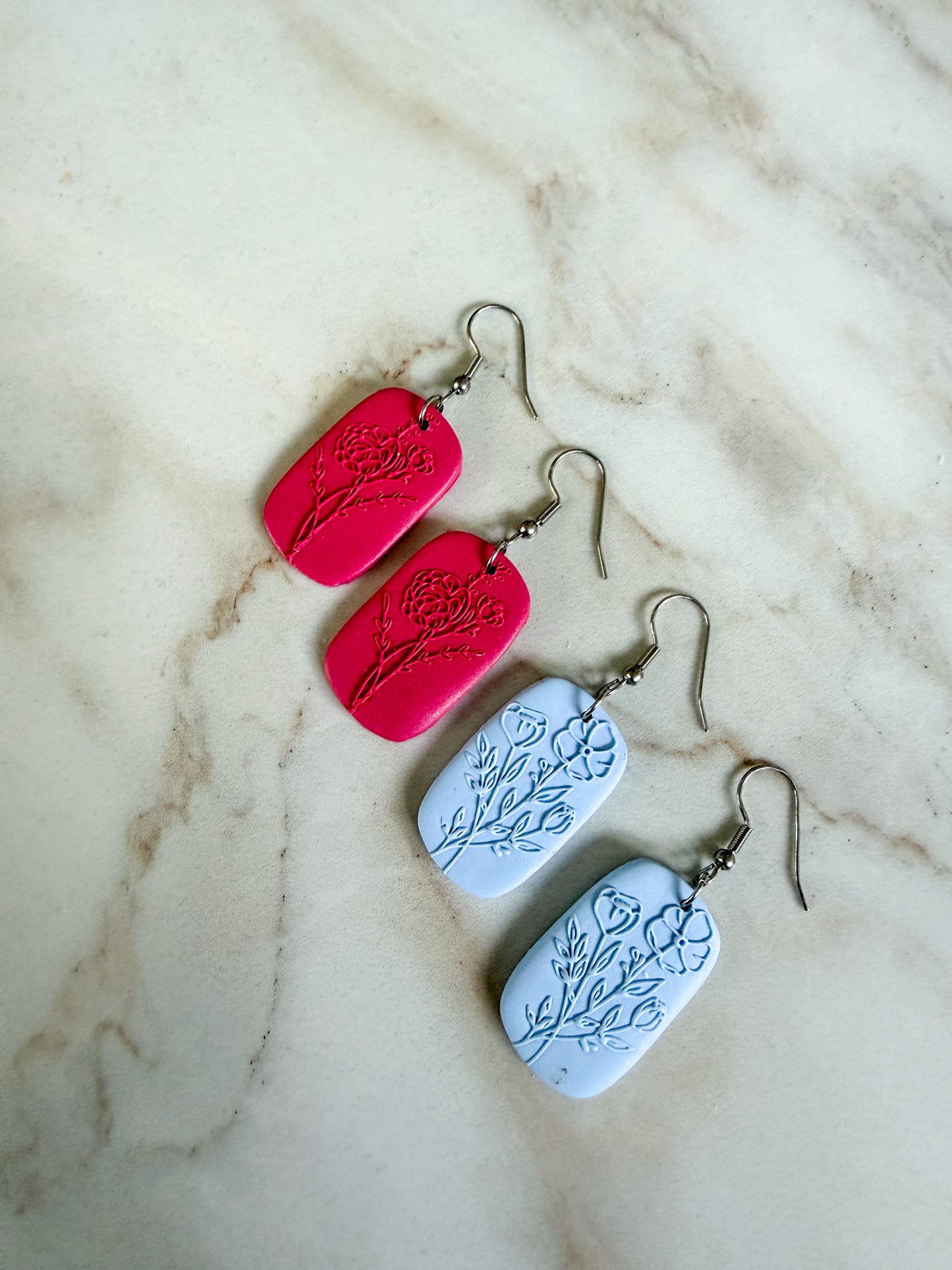 Pair of pink and blue earrings with floral designs on a marble surface