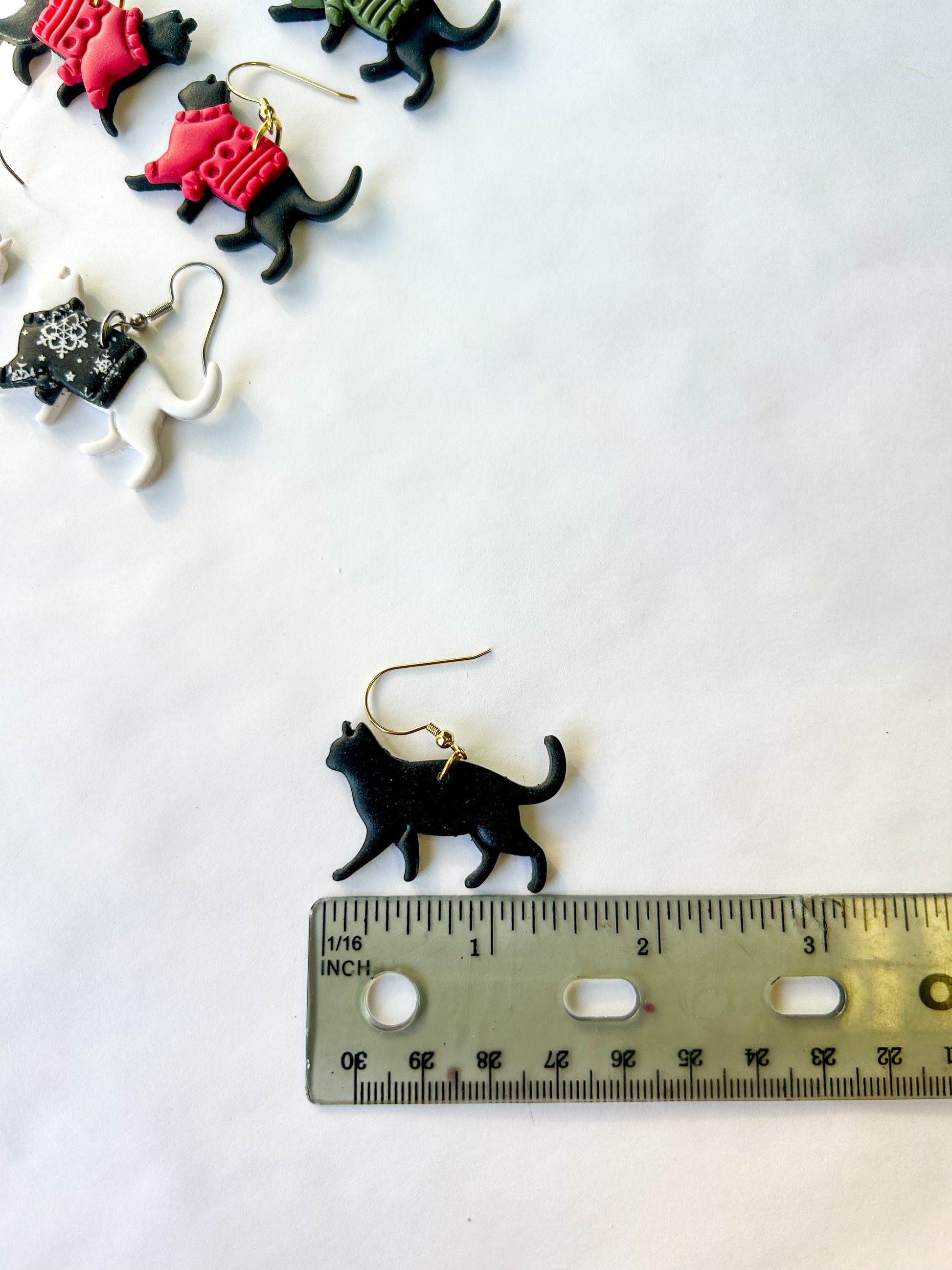 Black cat-shaped earrings with a ruler for scale on a white background. Earrings are about one and a half inches long